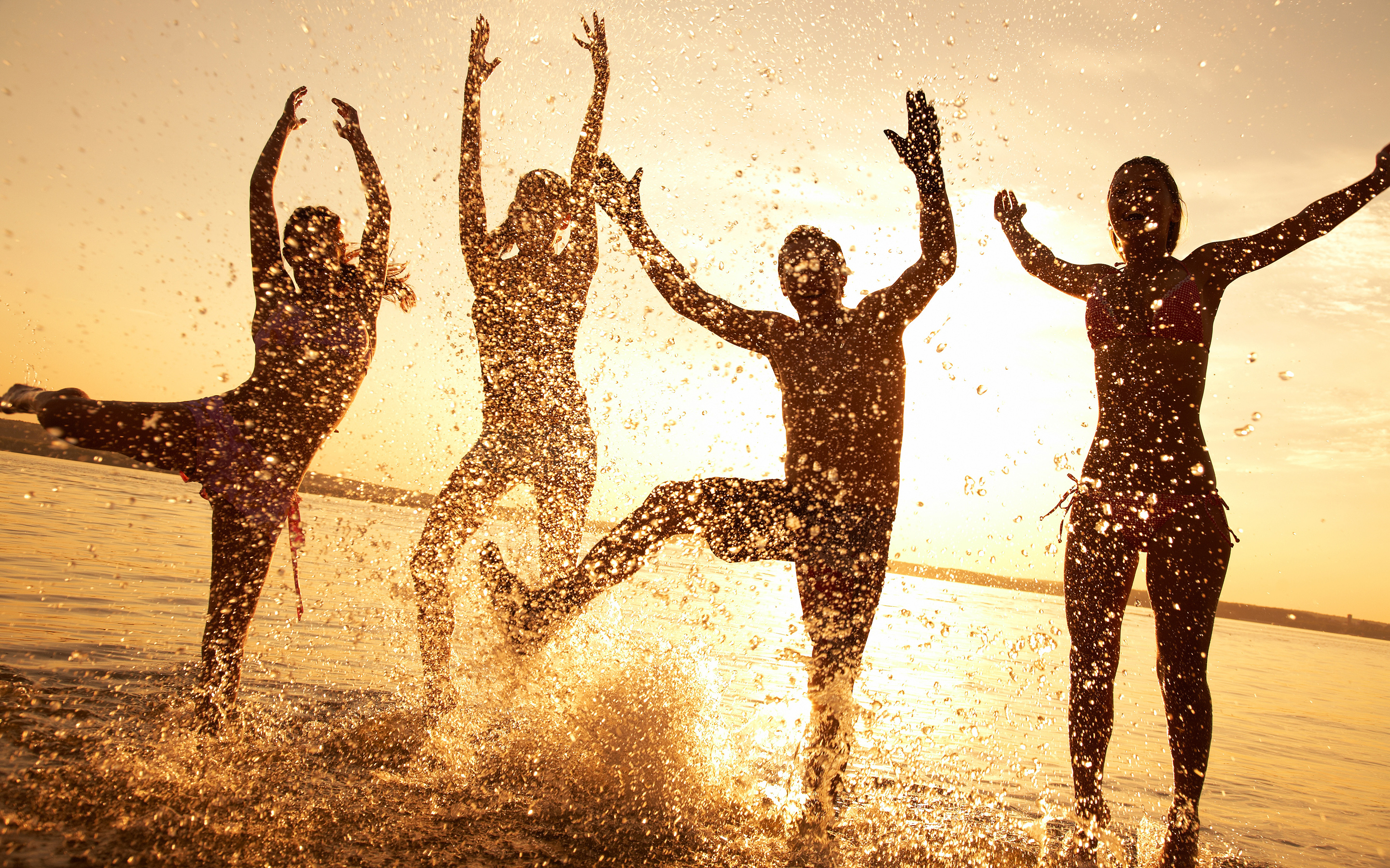 Four people jumping in water at sunset HD Wallpaper
