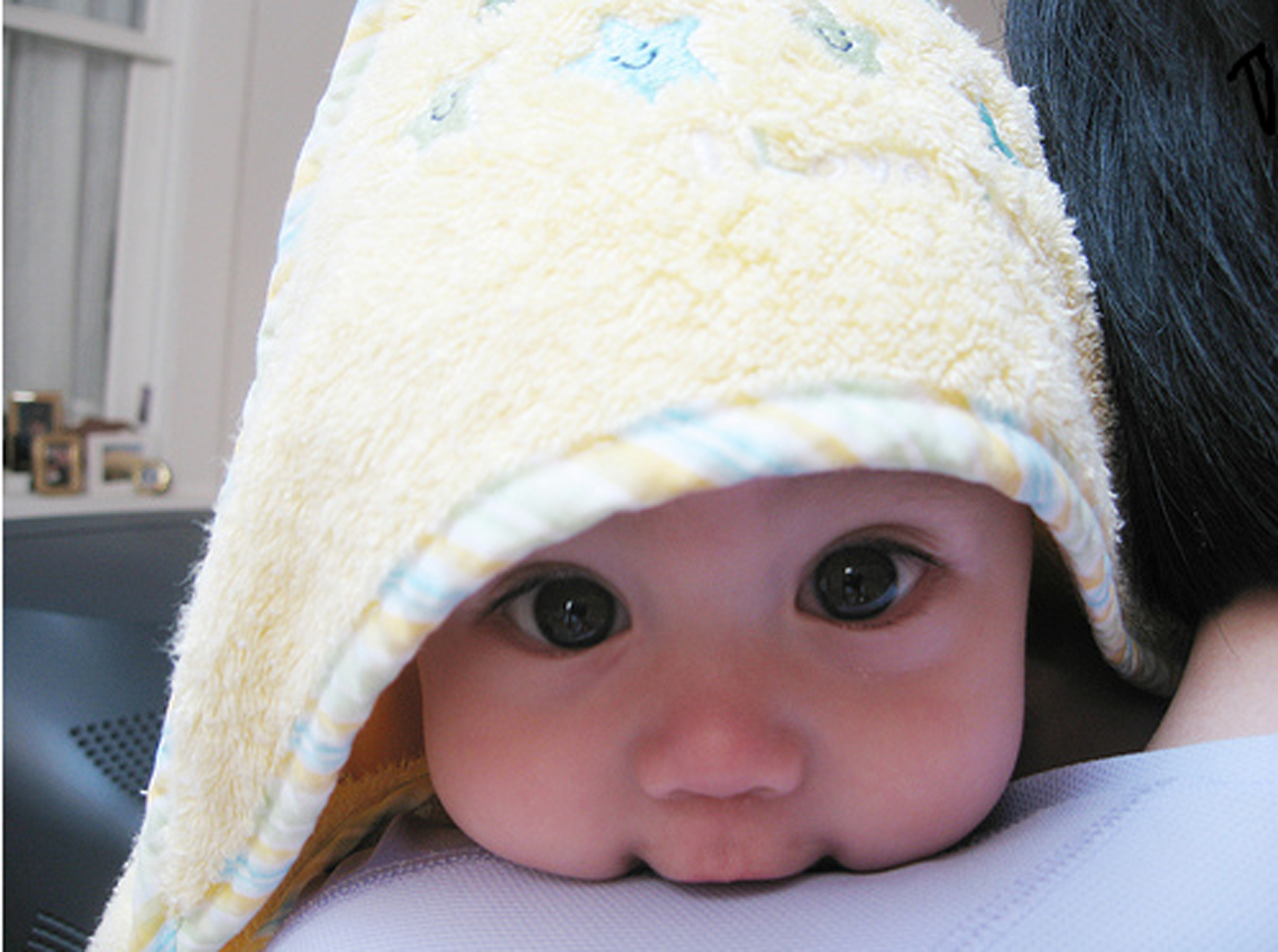 Baby peeking from under a yellow hooded towel HD Wallpaper