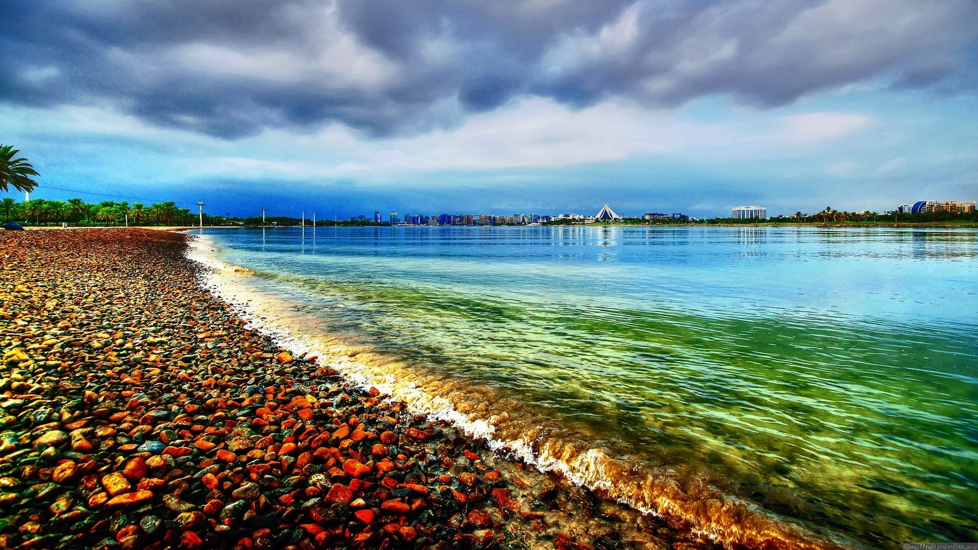 Pebble Beach with City Skyline and Stormy Sky HD Wallpaper