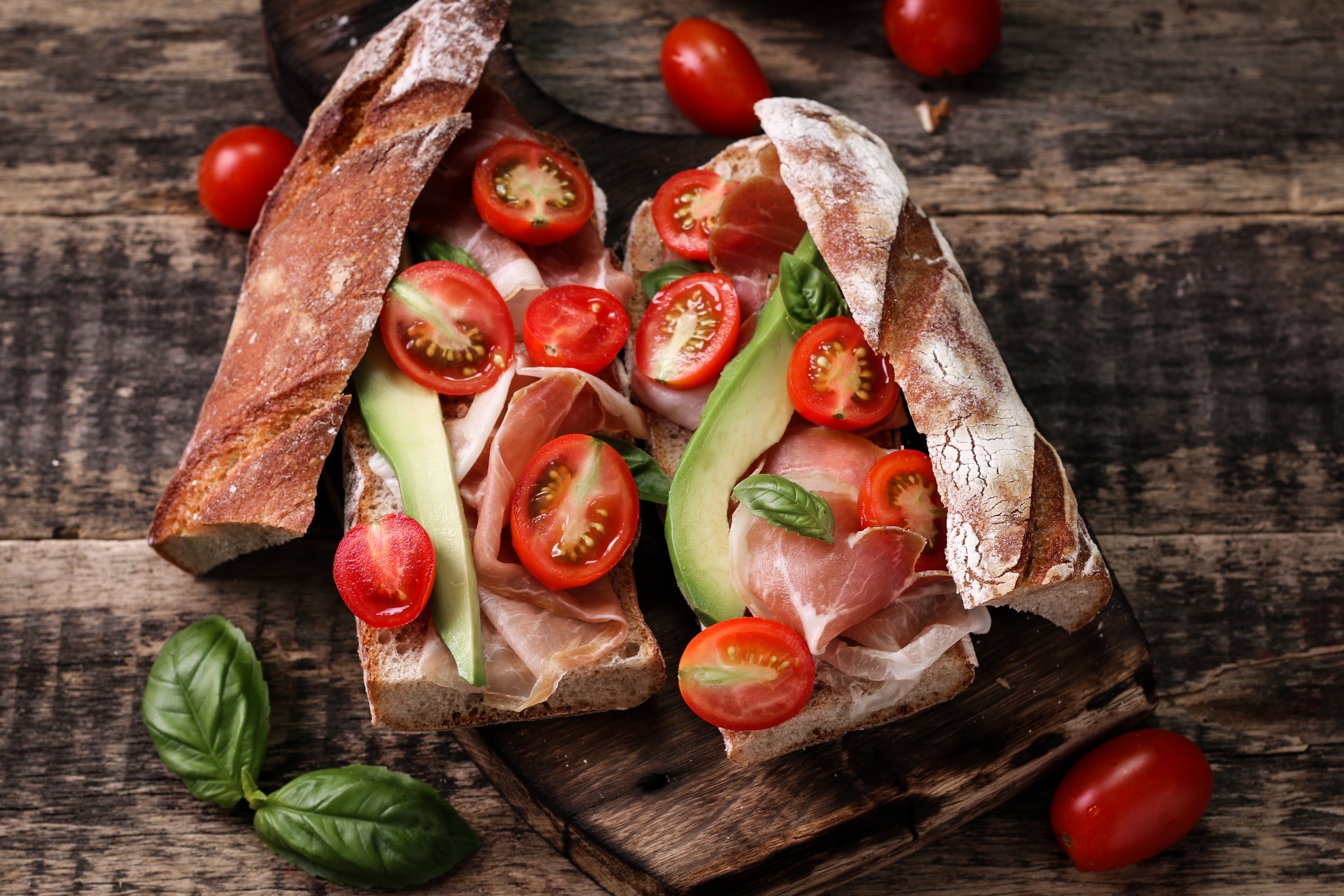 Sandwich with prosciutto, avocado, tomatoes, and basil on a wooden board HD Wallpaper
