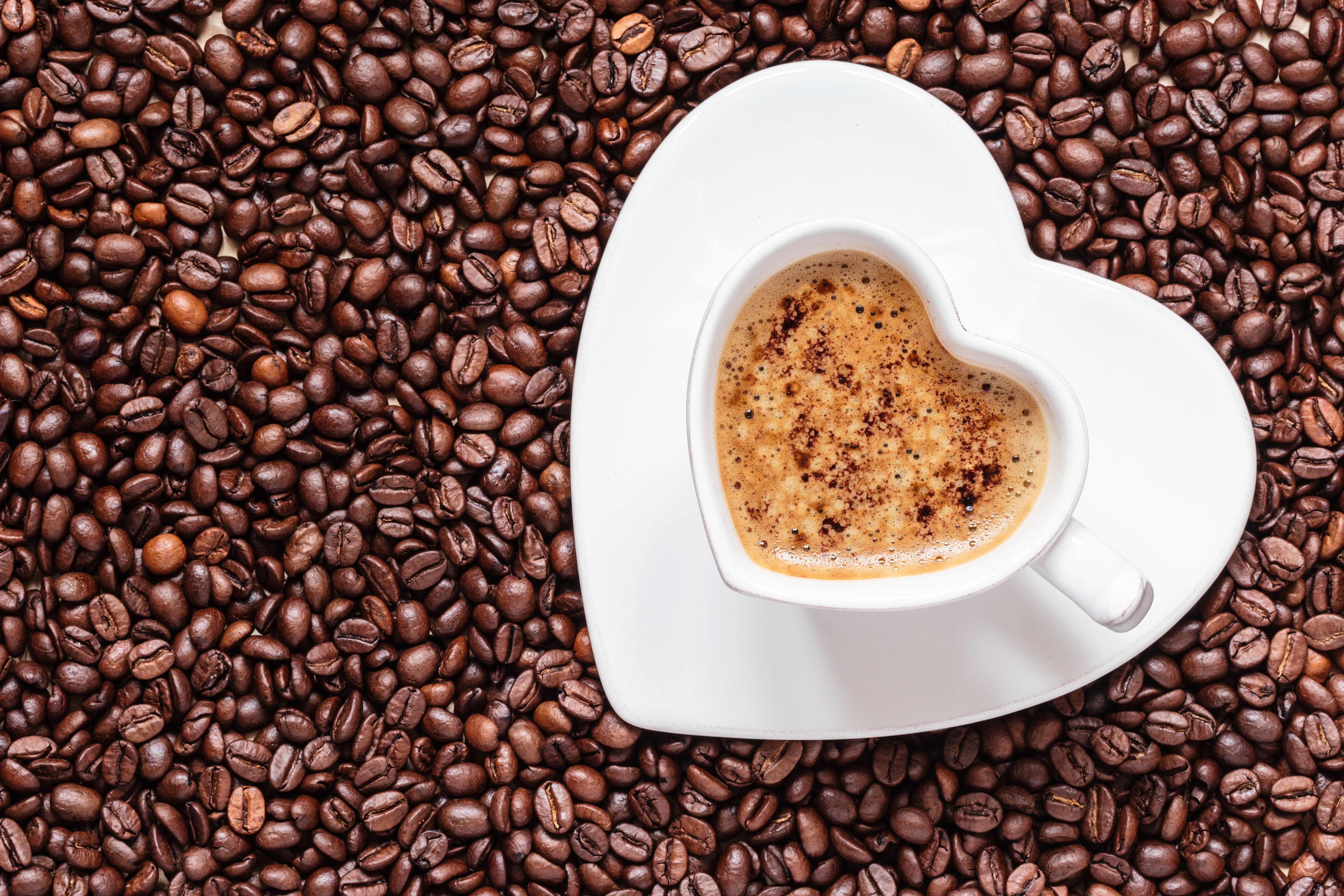 Heart-shaped cup of coffee on coffee beans HD Wallpaper