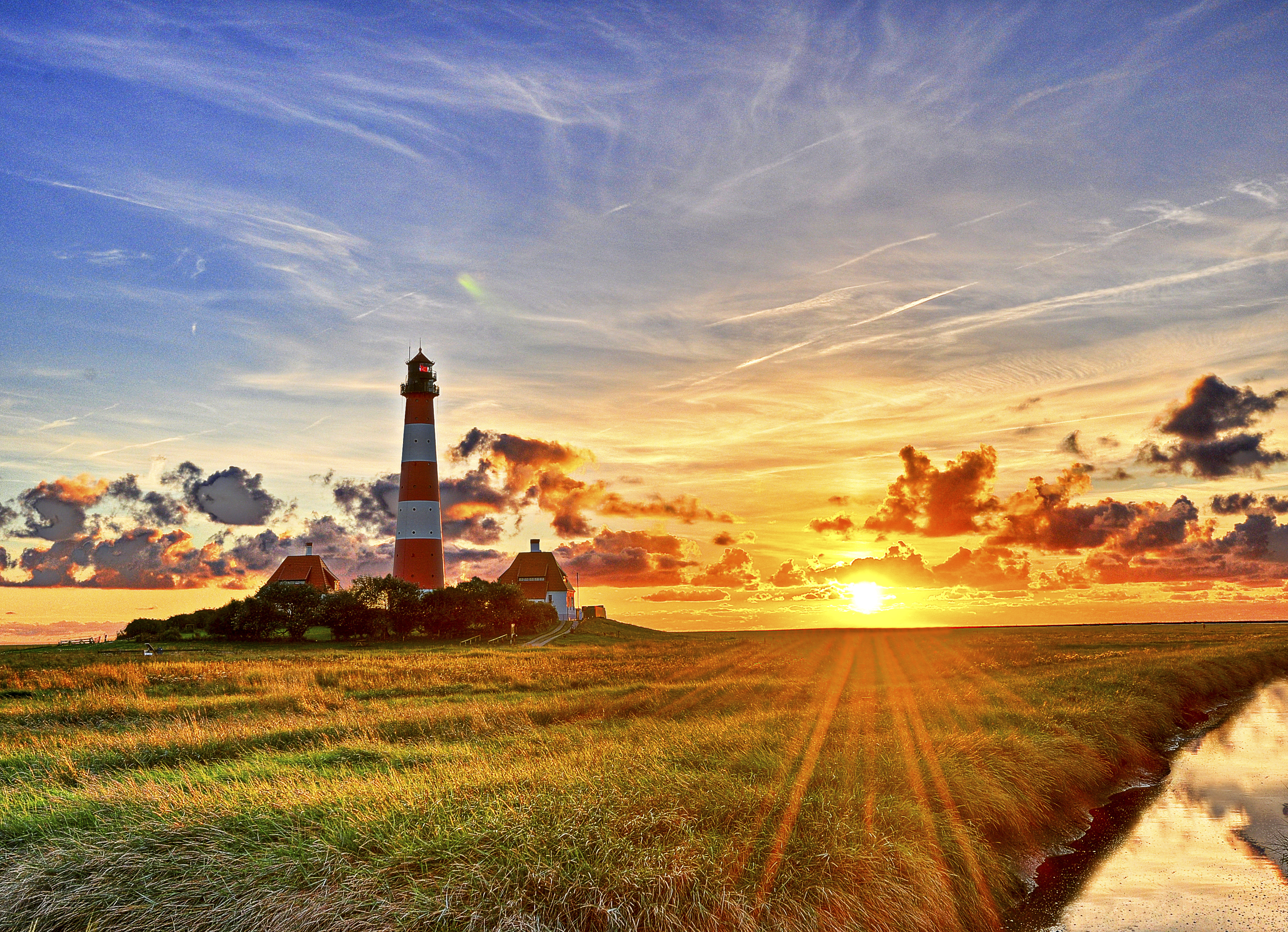 Lighthouse at sunset with sunbeams over grassy field HD Wallpaper