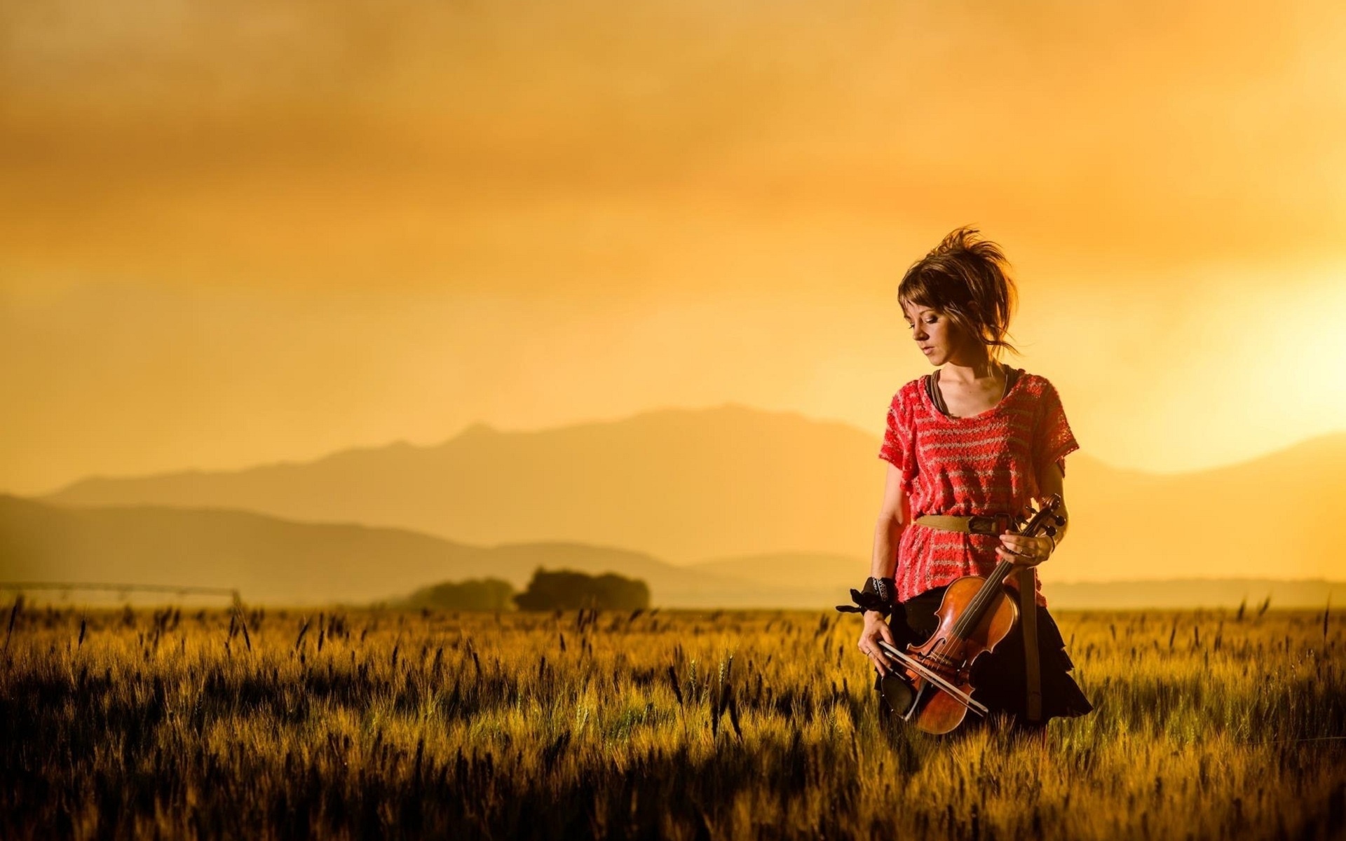 Lindsey Stirling with violin in a field at sunset HD Wallpaper