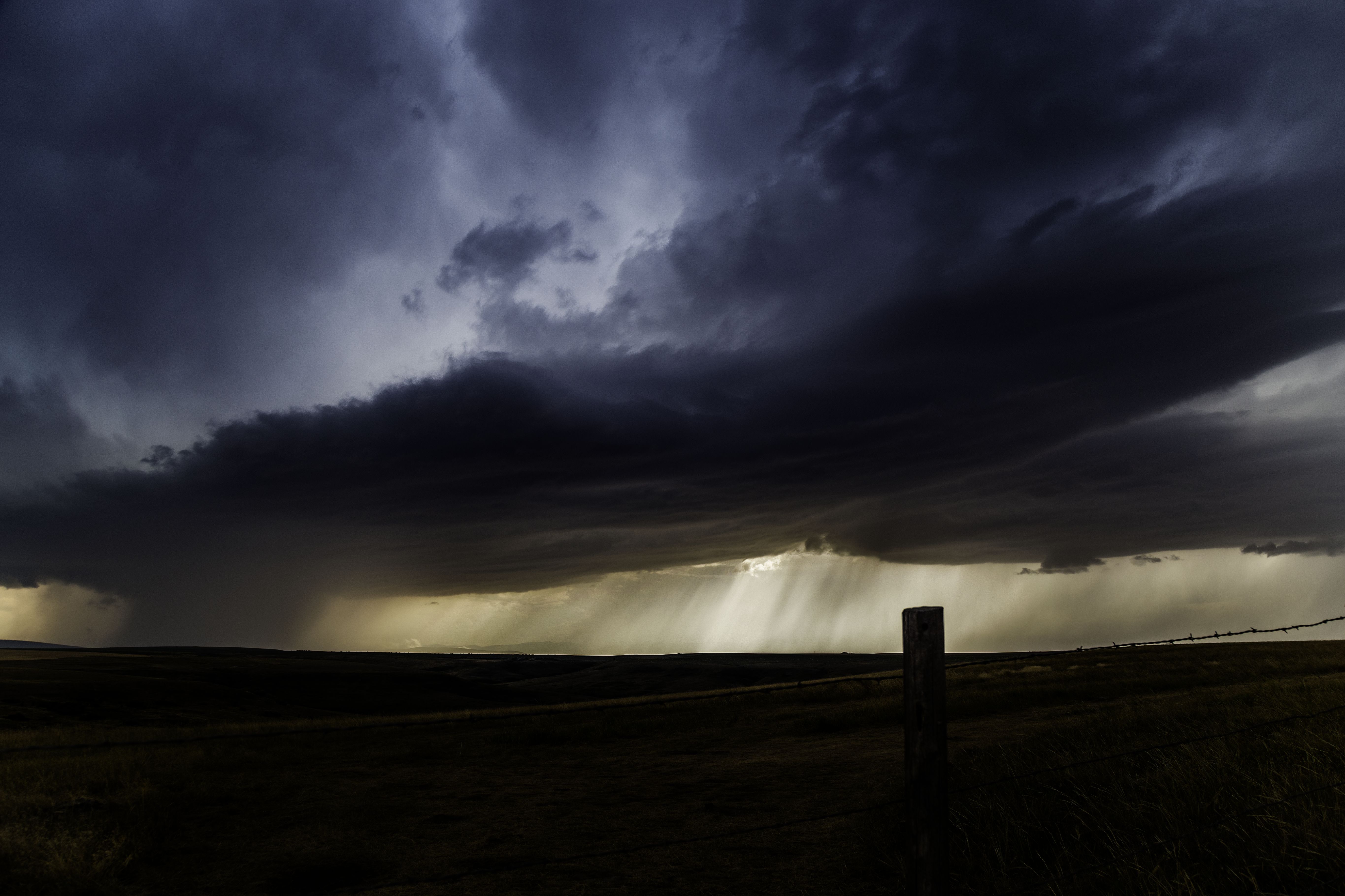 Stormy sky over a dark landscape with fence post HD Wallpaper