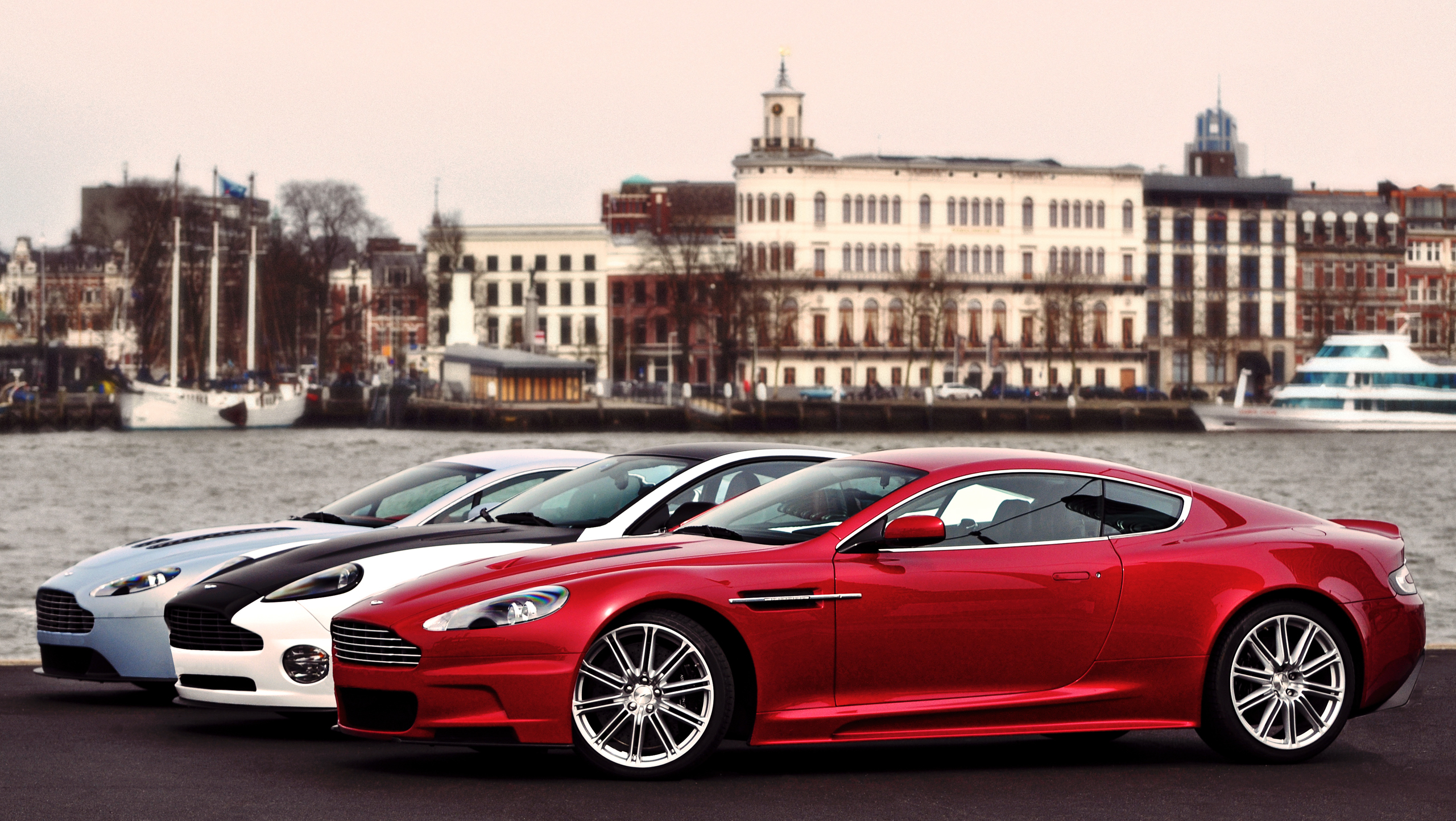 Aston Martin cars parked by a waterfront with buildings HD Wallpaper