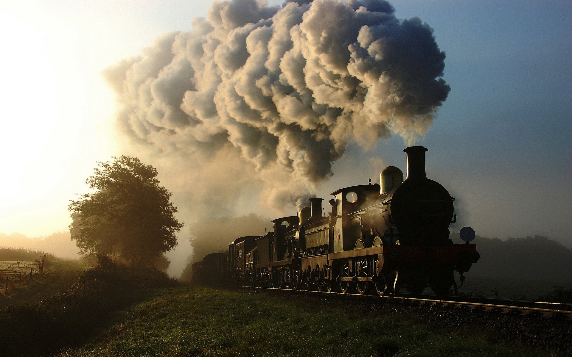 Steam locomotive emitting smoke in a rural landscape HD Wallpaper