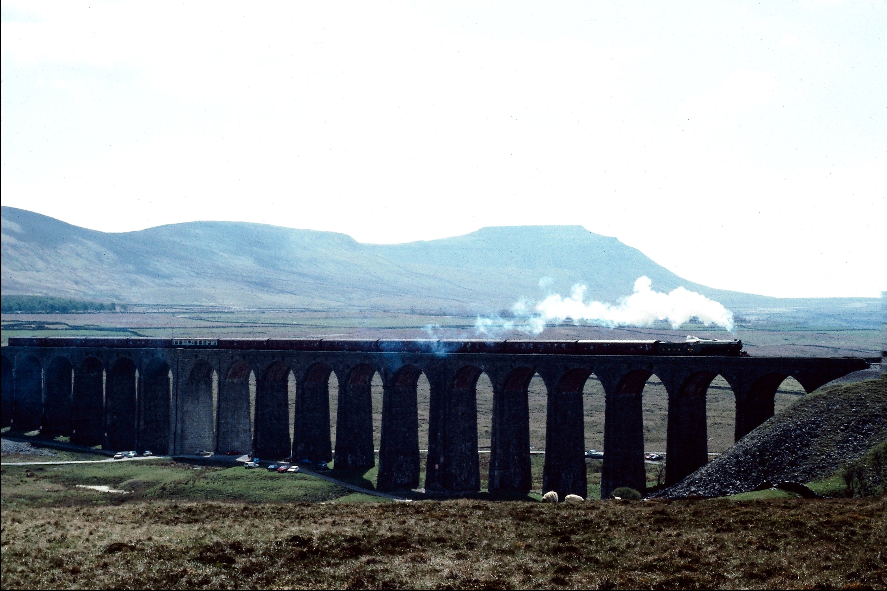 Steam train crossing a stone viaduct with mountains in background HD Wallpaper