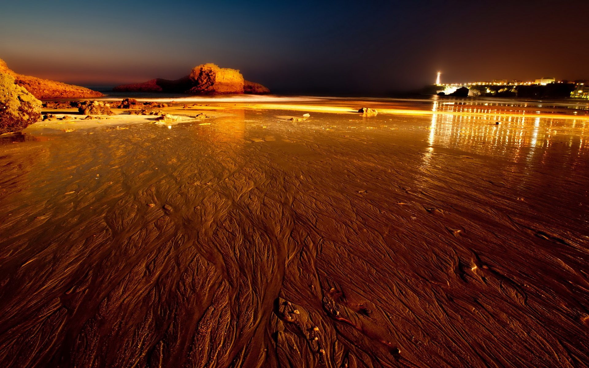 Beach at night with lighthouse and city lights in Biarritz, France HD Wallpaper