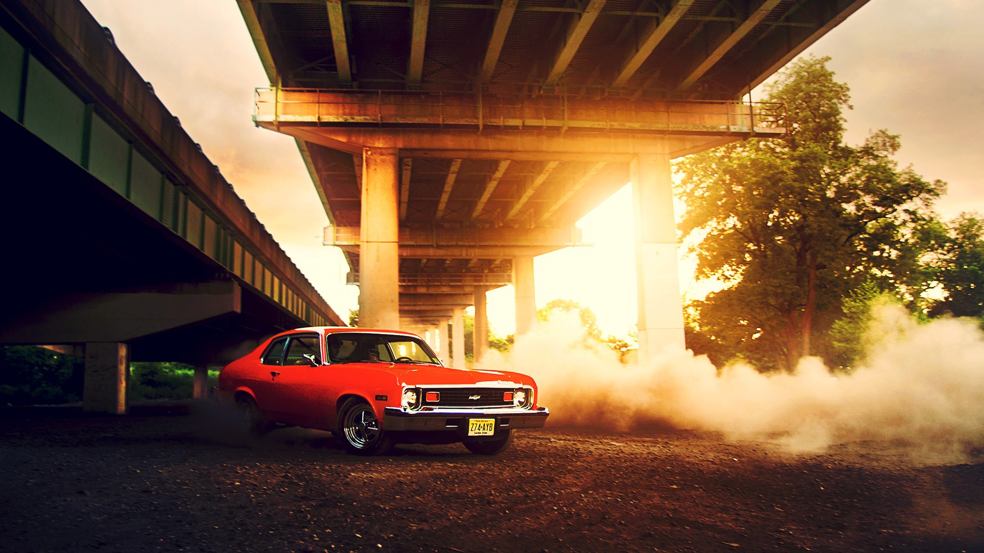 Red Chevrolet Nova doing a burnout under a bridge HD Wallpaper