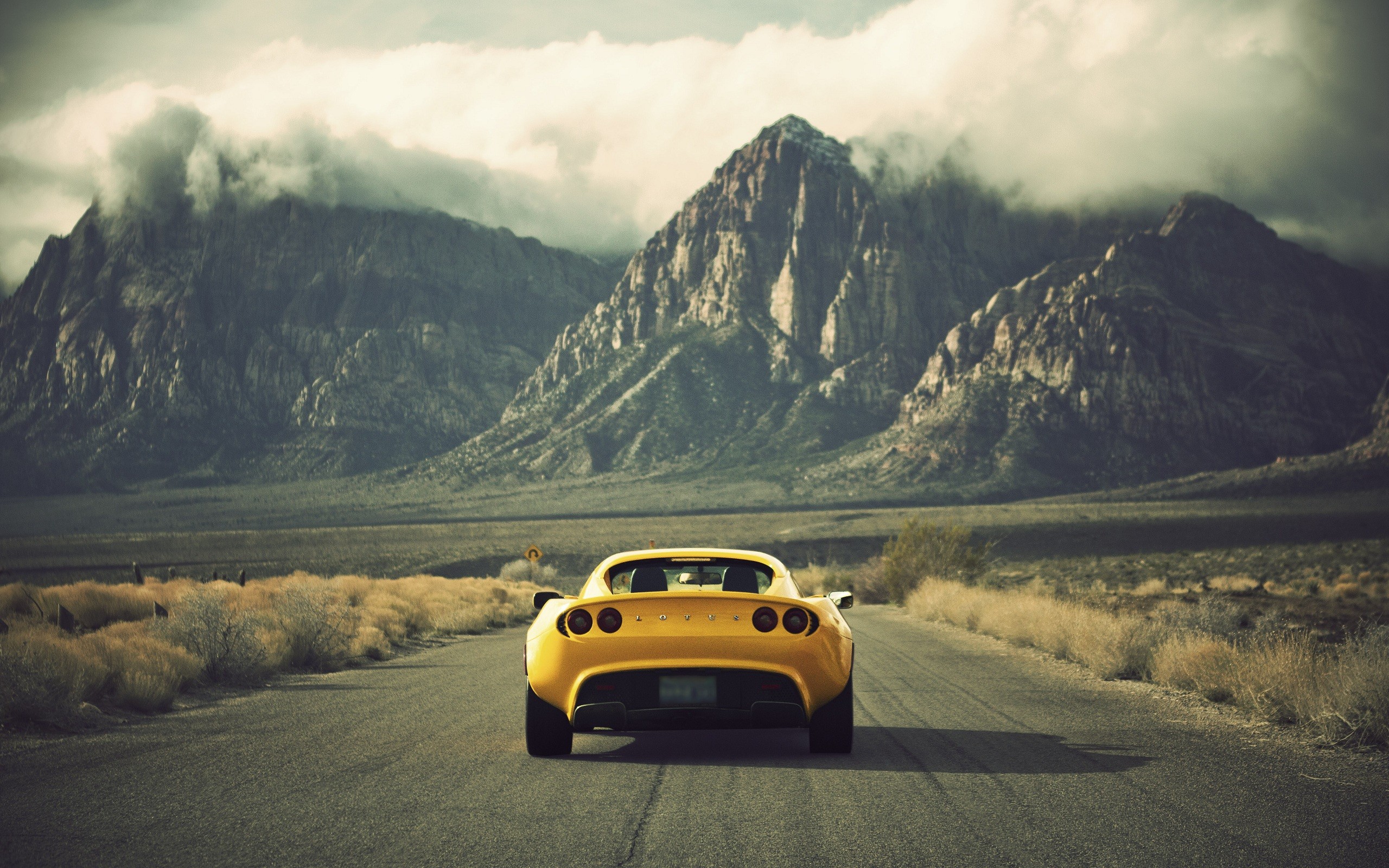 Yellow Lotus Car on a Desert Road with Mountains HD Wallpaper