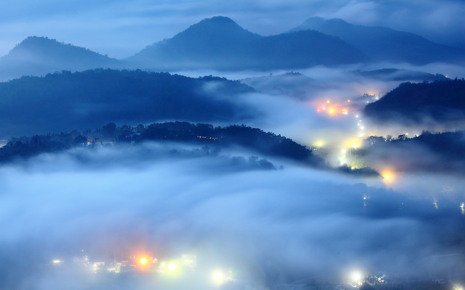 Mountains shrouded in fog with village lights HD Wallpaper