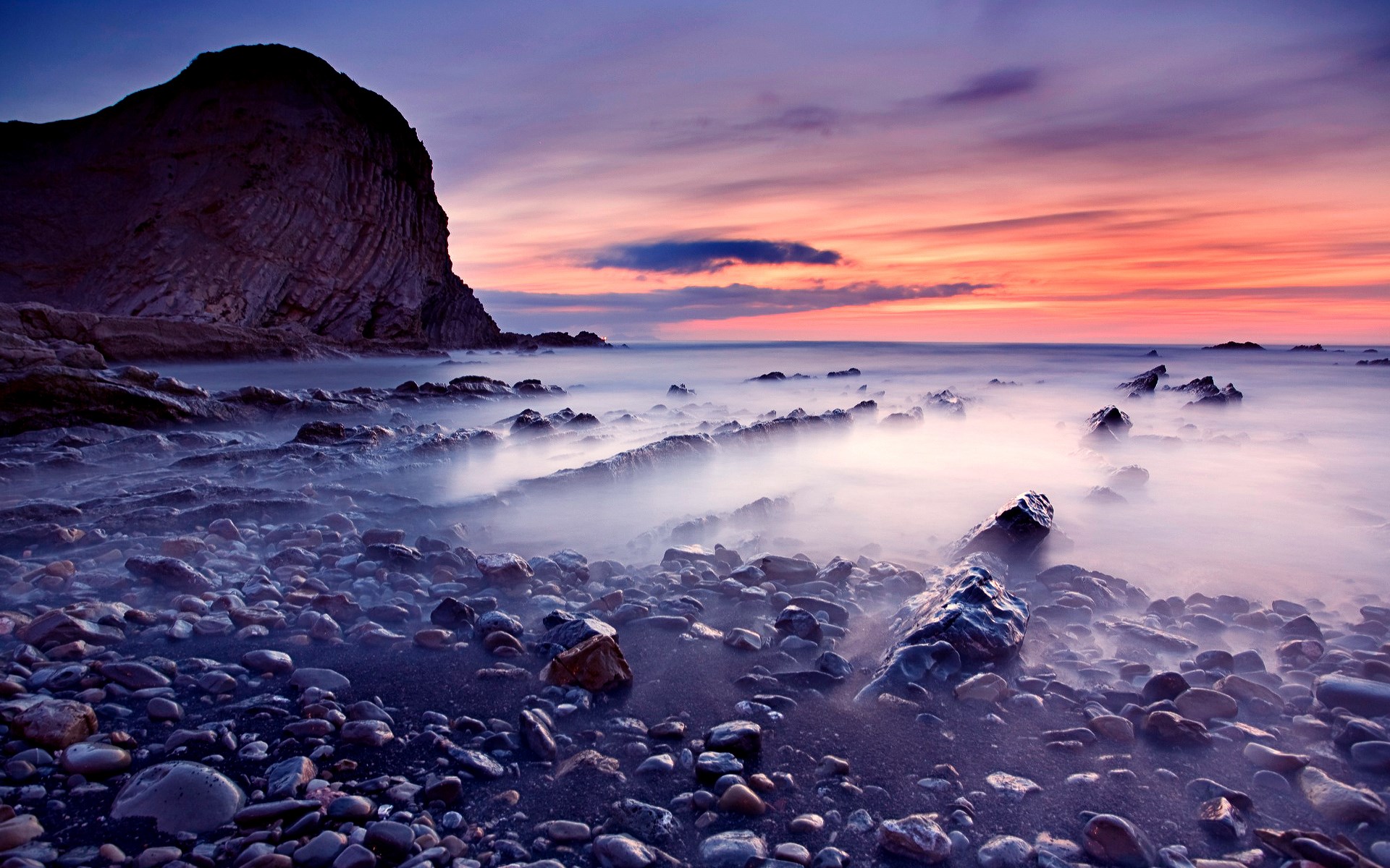 Rocky coastline at sunset with misty ocean HD Wallpaper