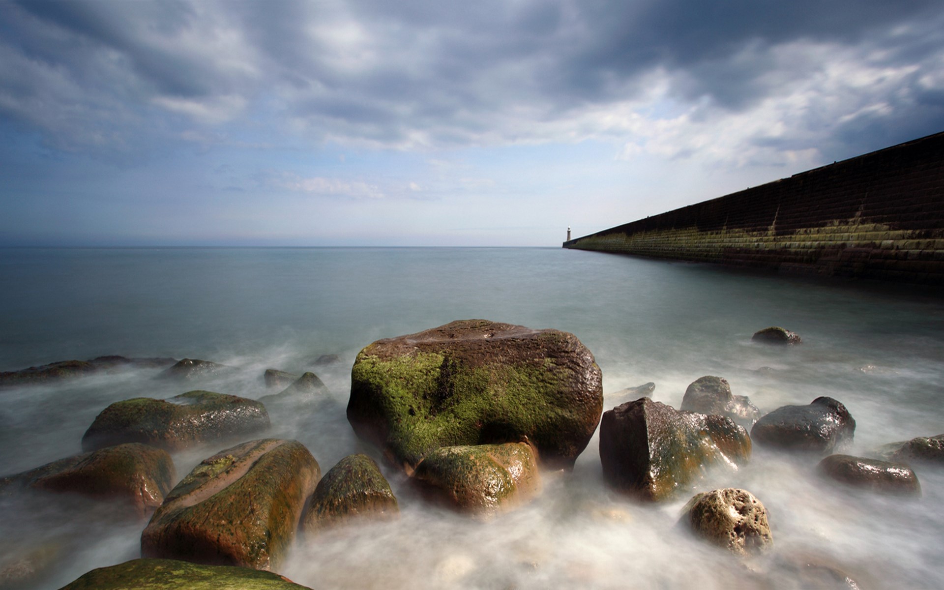 Long exposure of a rocky shore with a breakwater and lighthouse HD Wallpaper