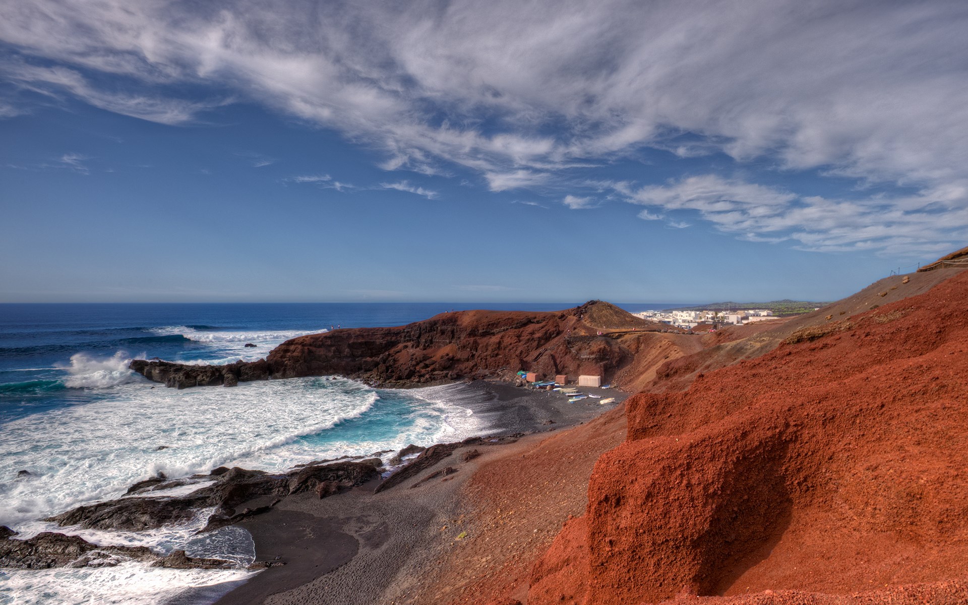 Red volcanic cliffs and black sand beach with ocean waves HD Wallpaper