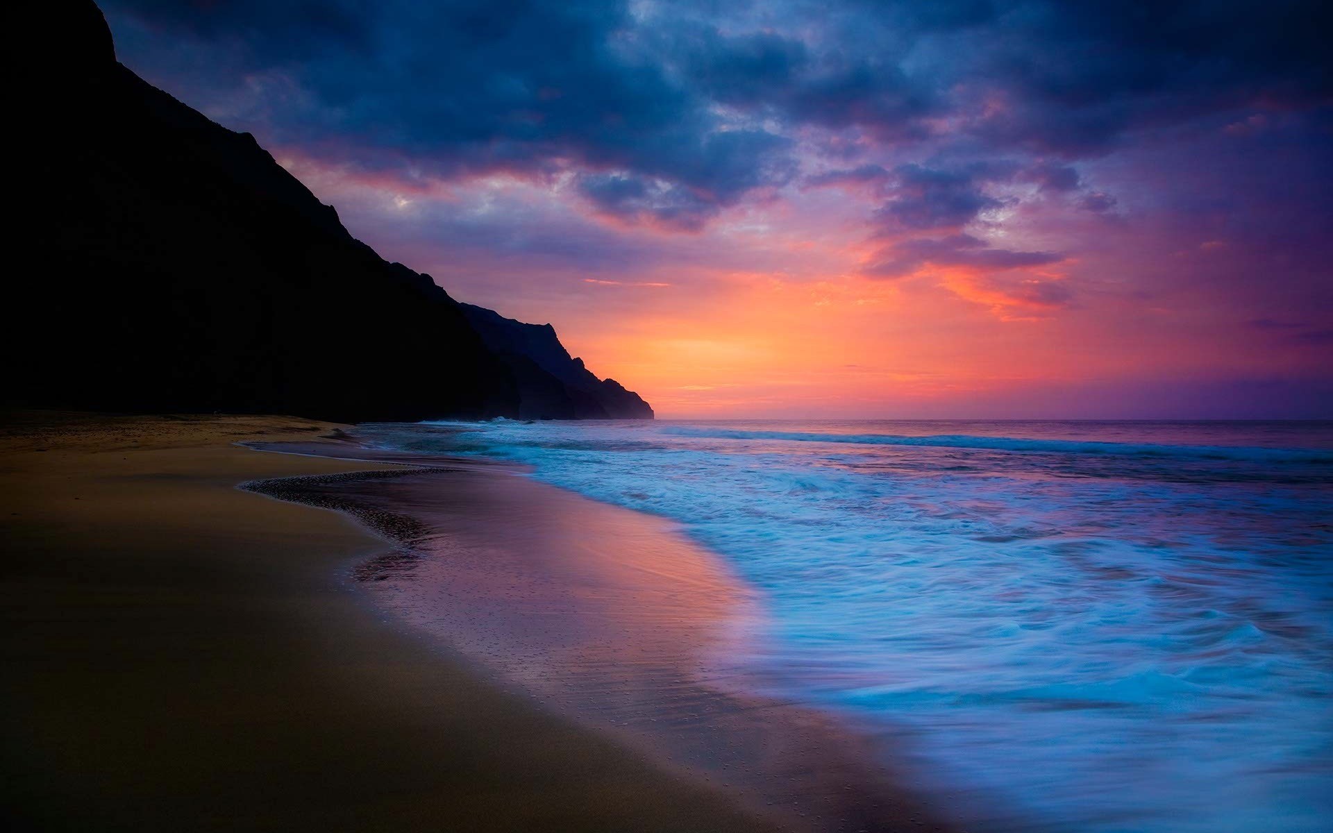Sunset over a beach with dark mountains and ocean waves HD Wallpaper
