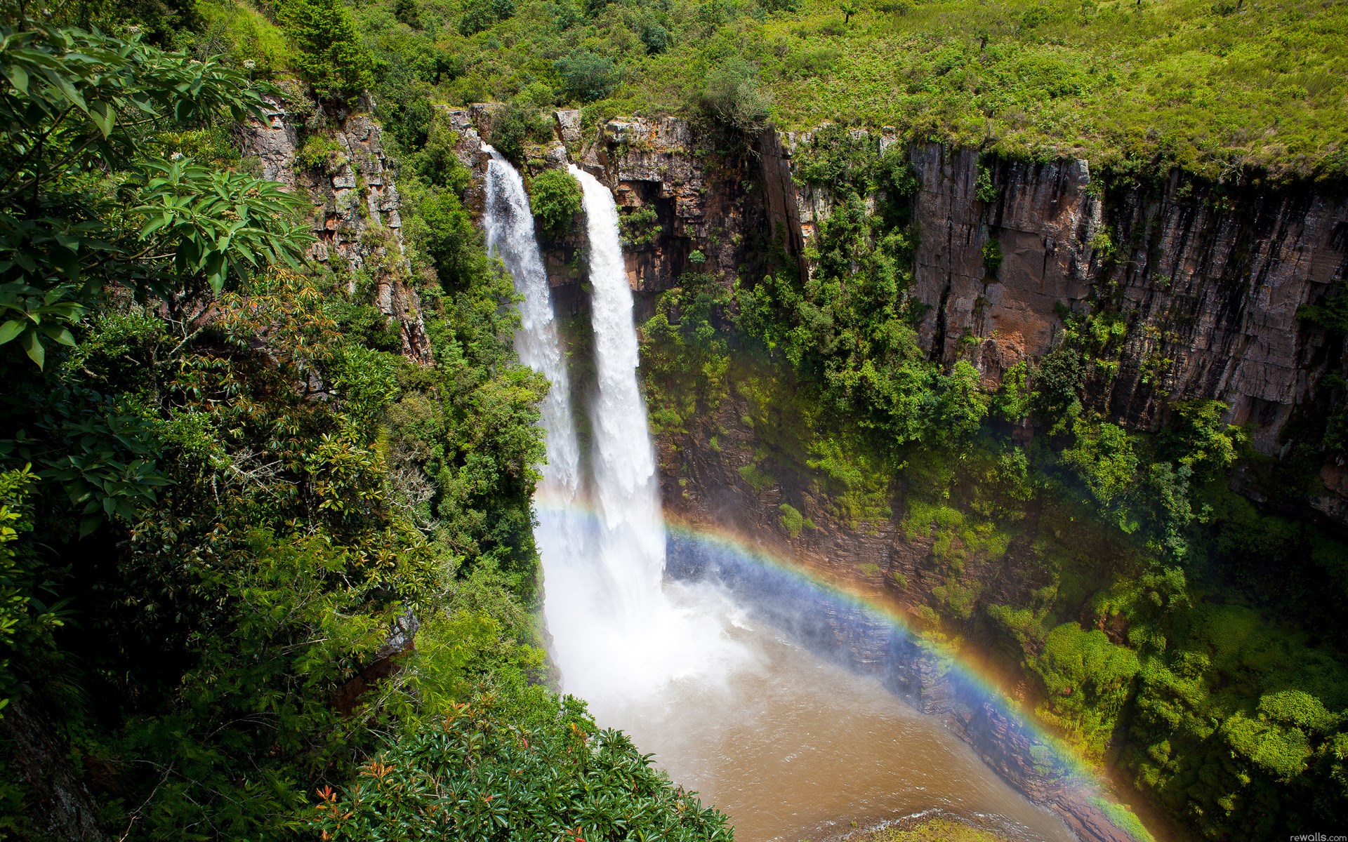 Waterfall with a rainbow in a lush green canyon HD Wallpaper