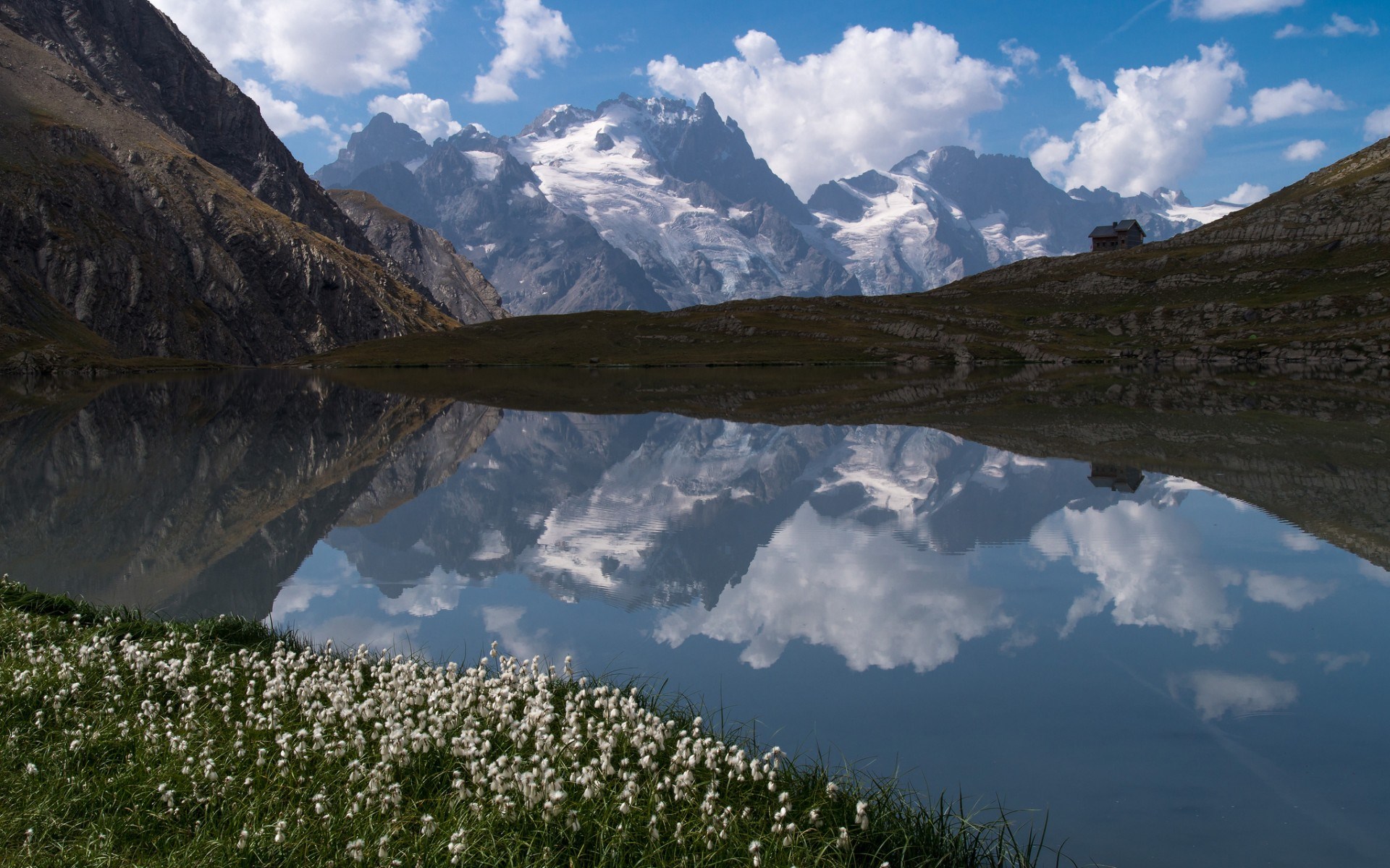 Mountain lake reflecting snow-capped peaks and a small cabin HD Wallpaper