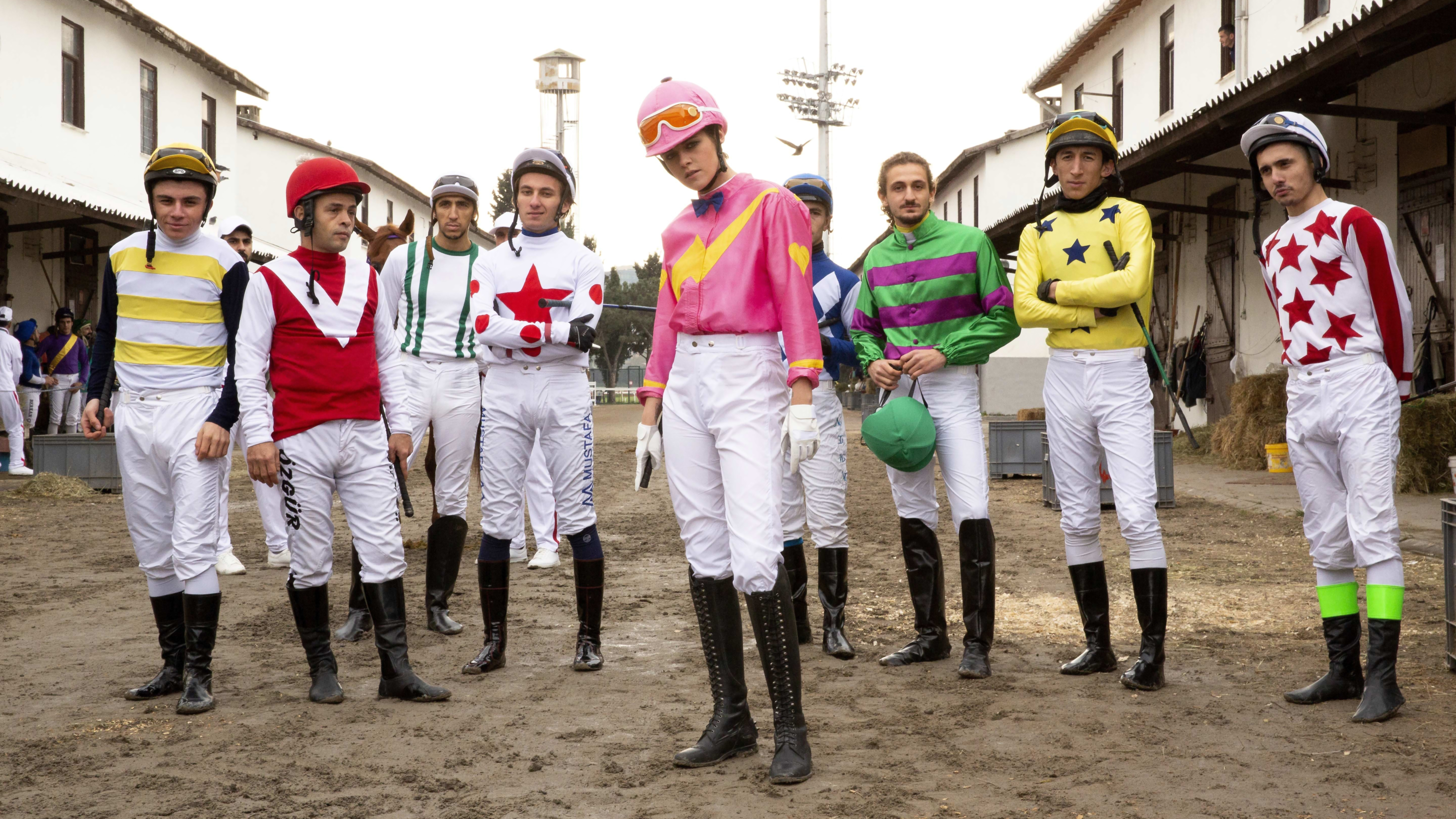 Group of jockeys in colorful racing silks standing outside stables HD Wallpaper