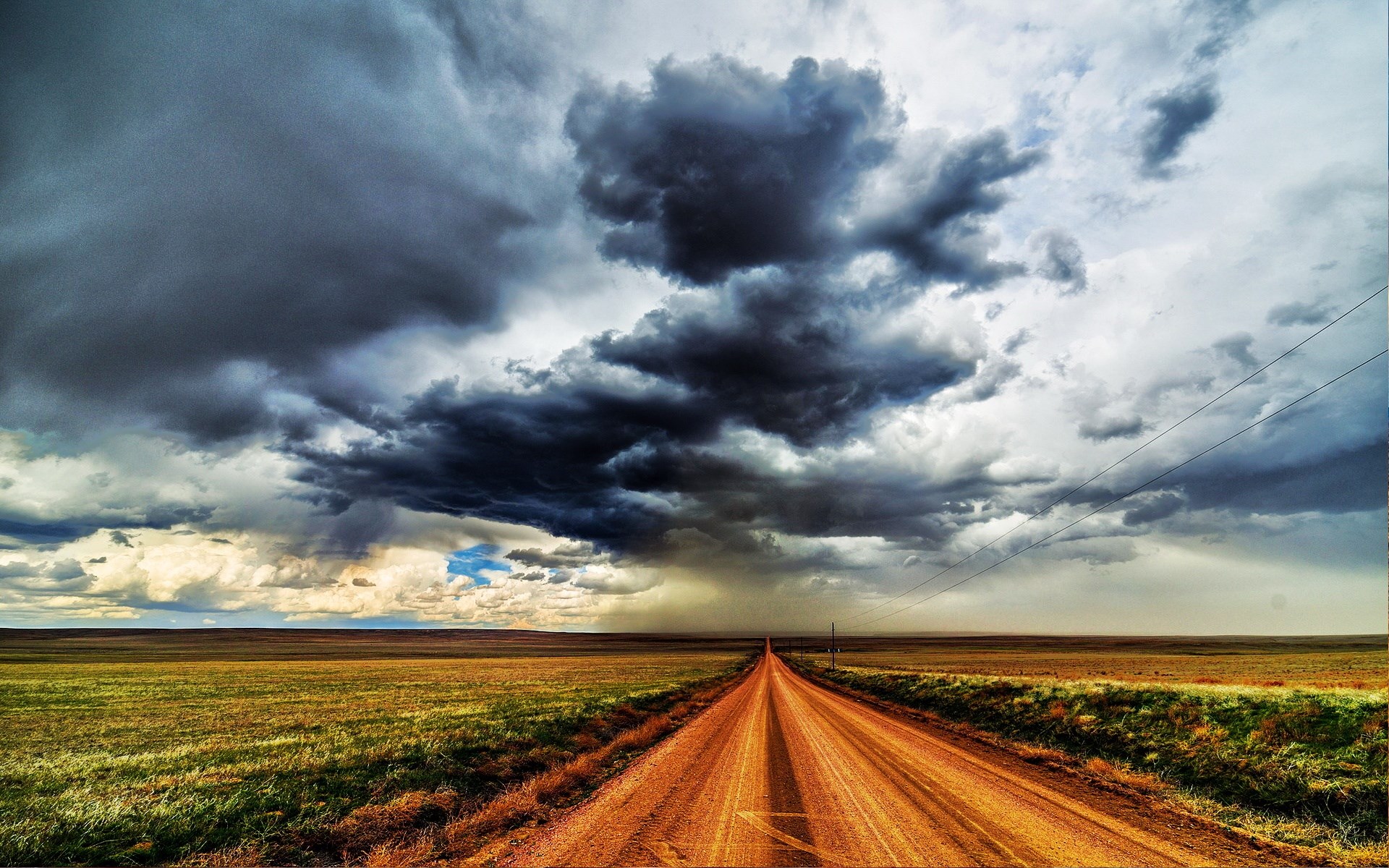 Dirt road leading through a field under stormy clouds HD Wallpaper