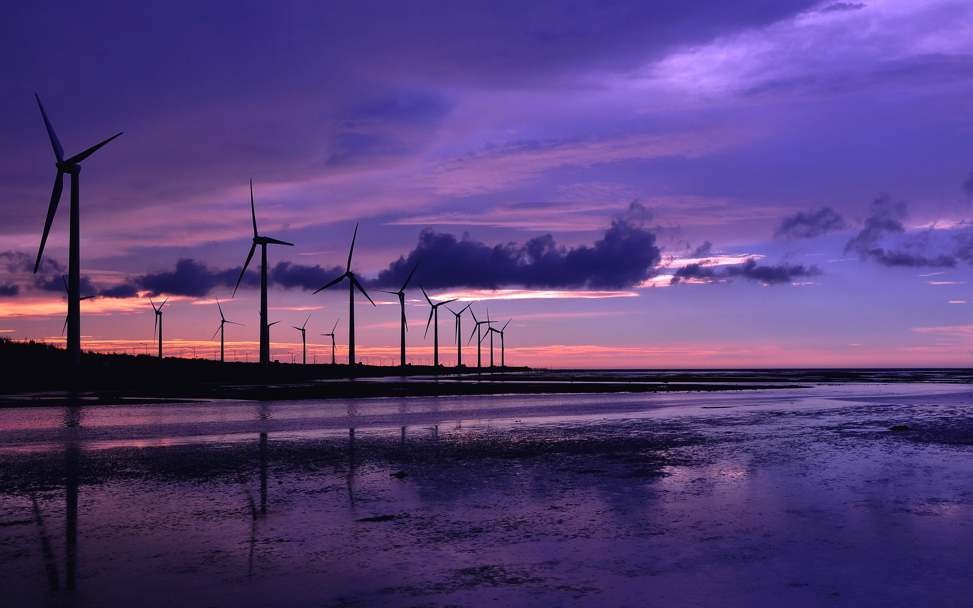 Wind turbines silhouetted against a purple sunset over water HD Wallpaper