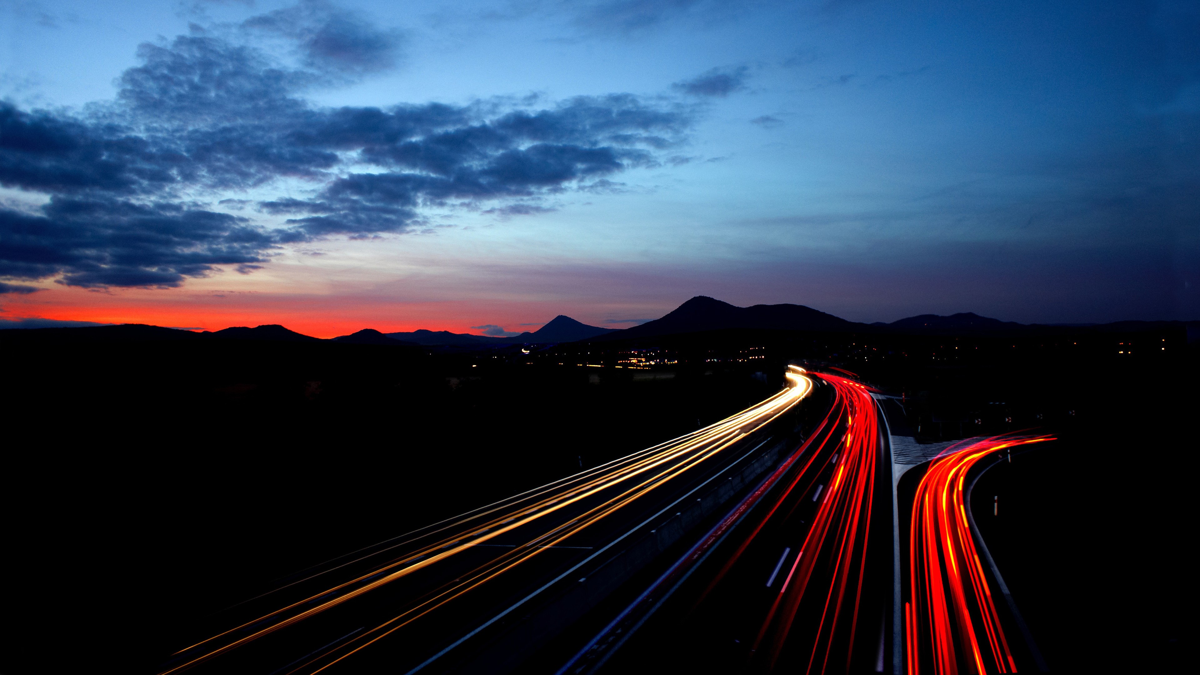 Highway light trails at sunset with mountains HD Wallpaper