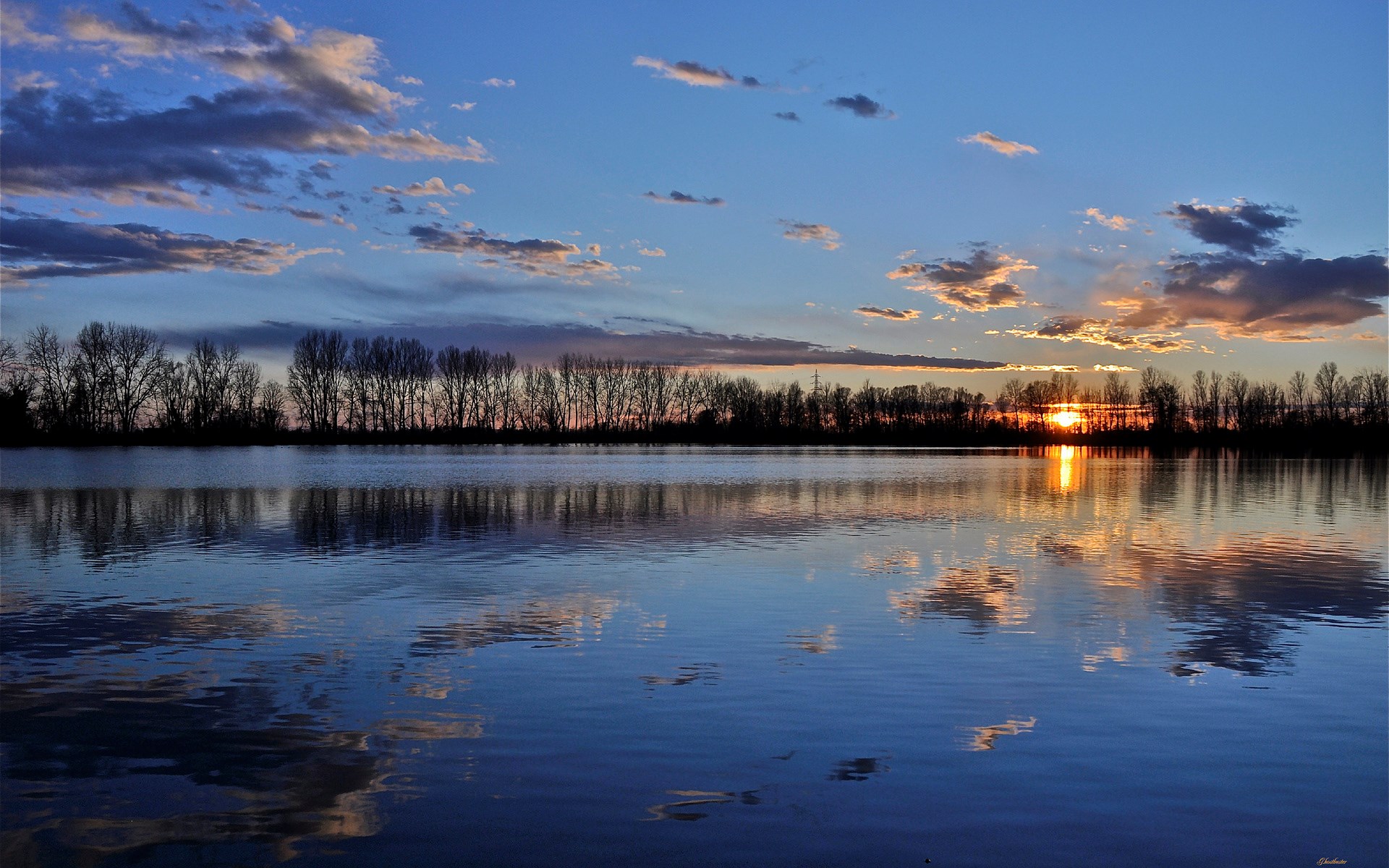 Sunset over a calm lake with trees and clouds reflected HD Wallpaper