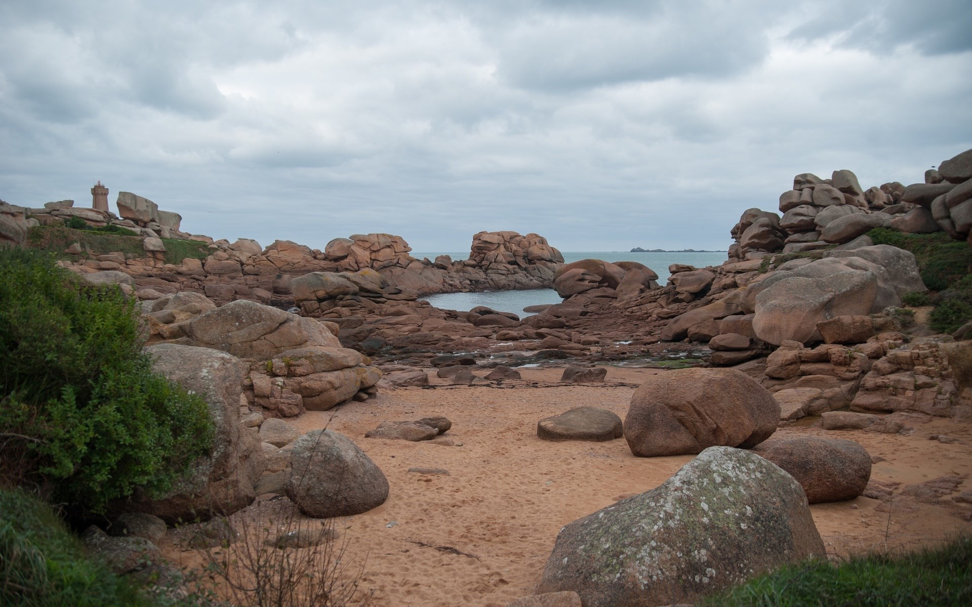 Pink granite boulders on a sandy beach with a lighthouse HD Wallpaper