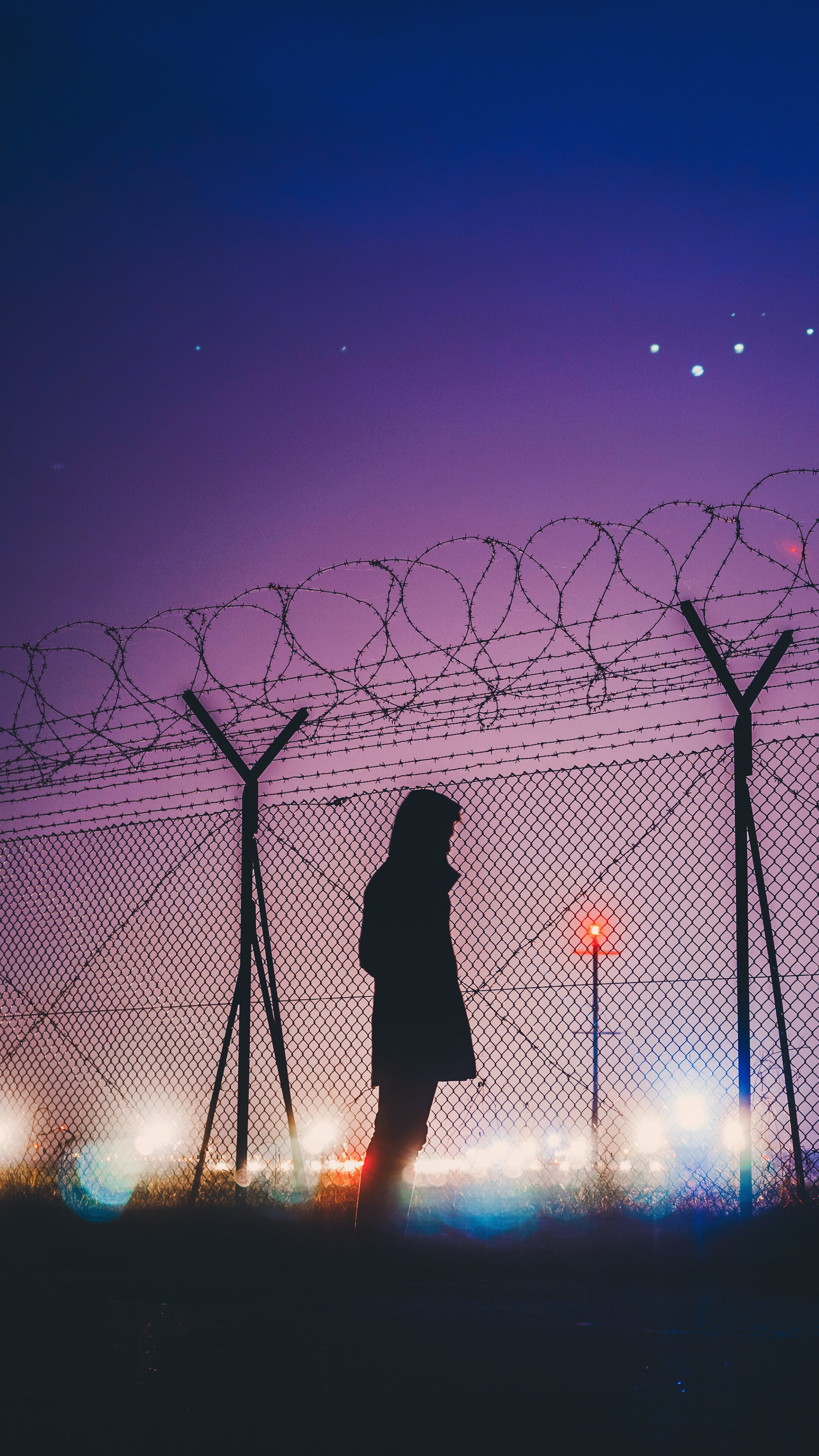 Silhouette of a person by a barbed wire fence at night HD Phone Wallpaper
