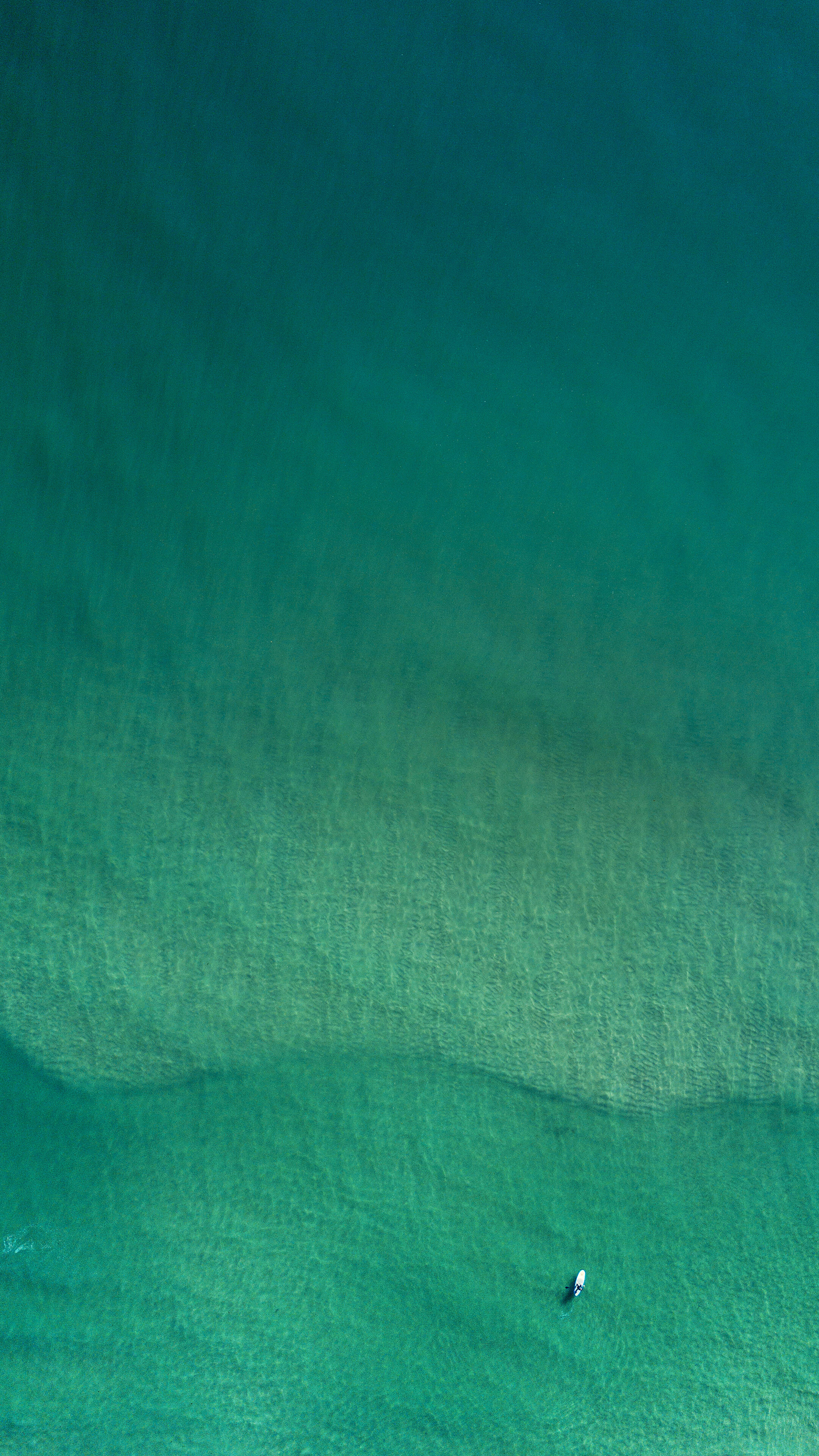 Aerial view of a person on a surfboard in clear turquoise water HD Phone Wallpaper