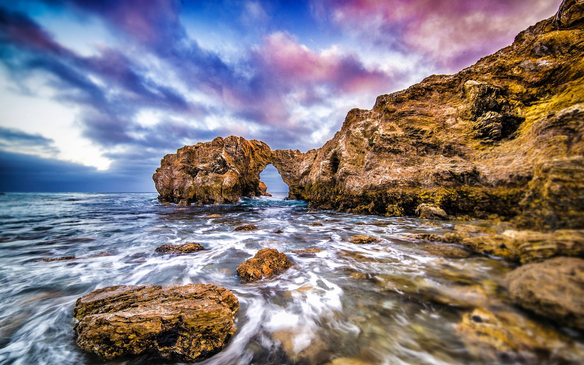 Ocean waves crashing against rock formations with arch HD Wallpaper
