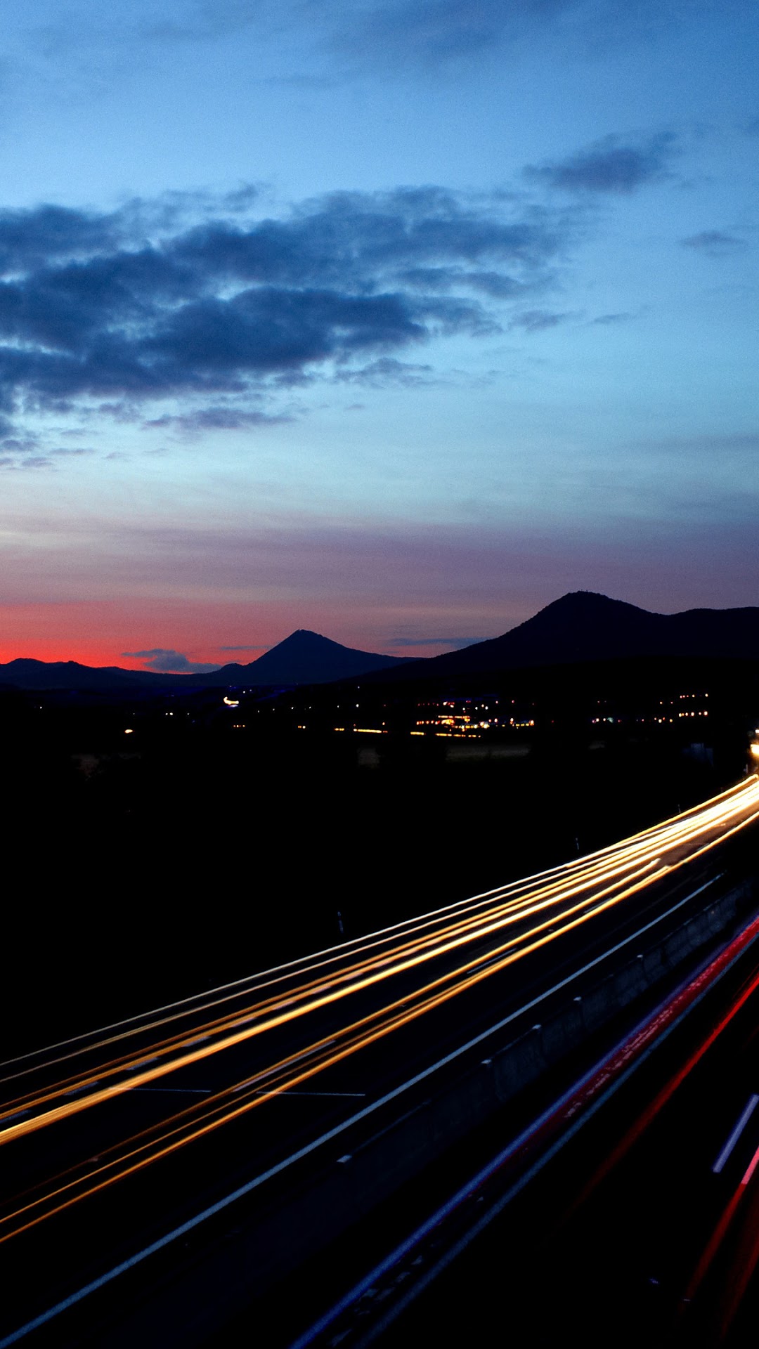Light trails on a highway at sunset with mountains HD Phone Wallpaper