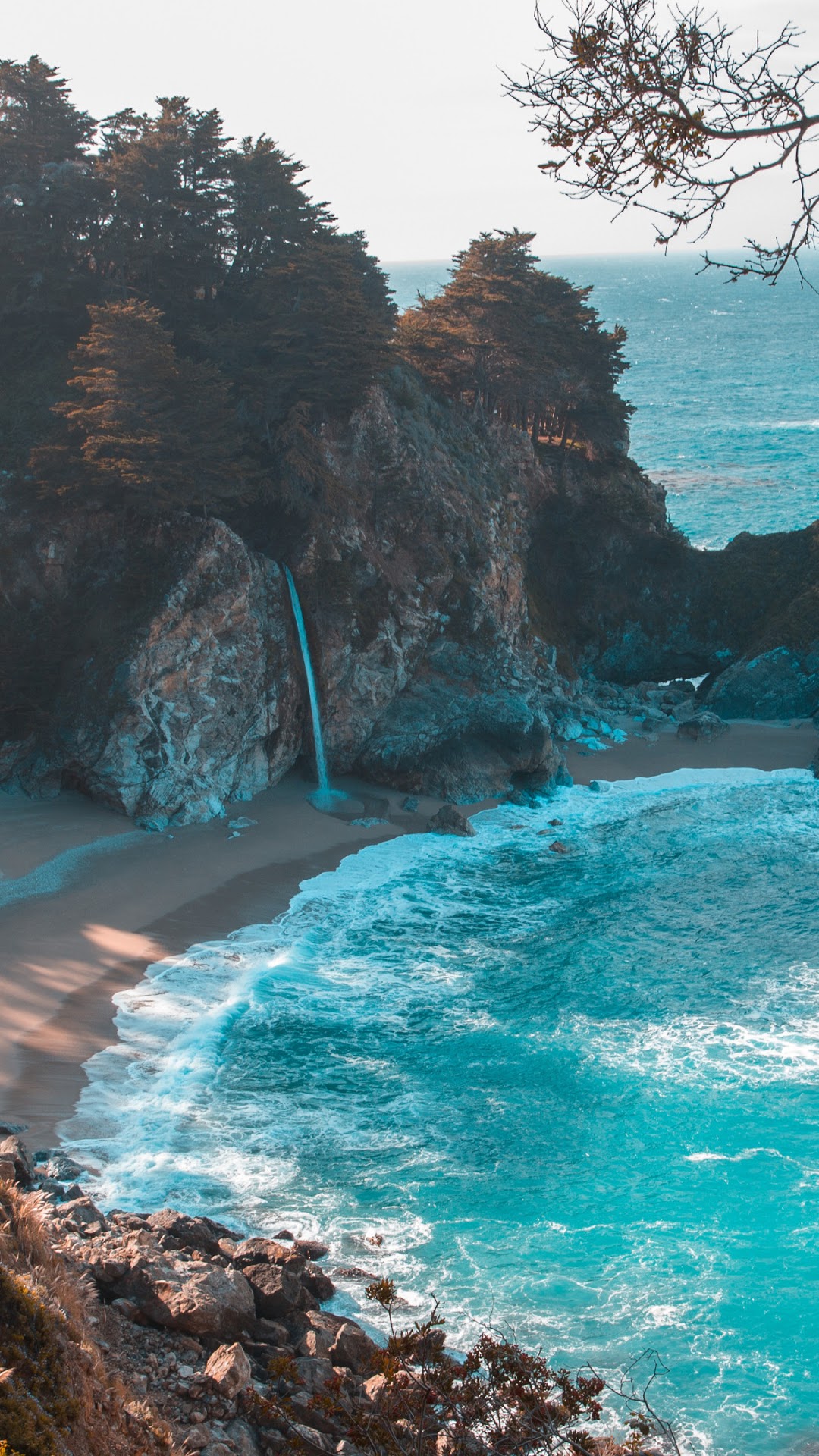 Waterfall cascading onto a sandy beach by the ocean HD Phone Wallpaper
