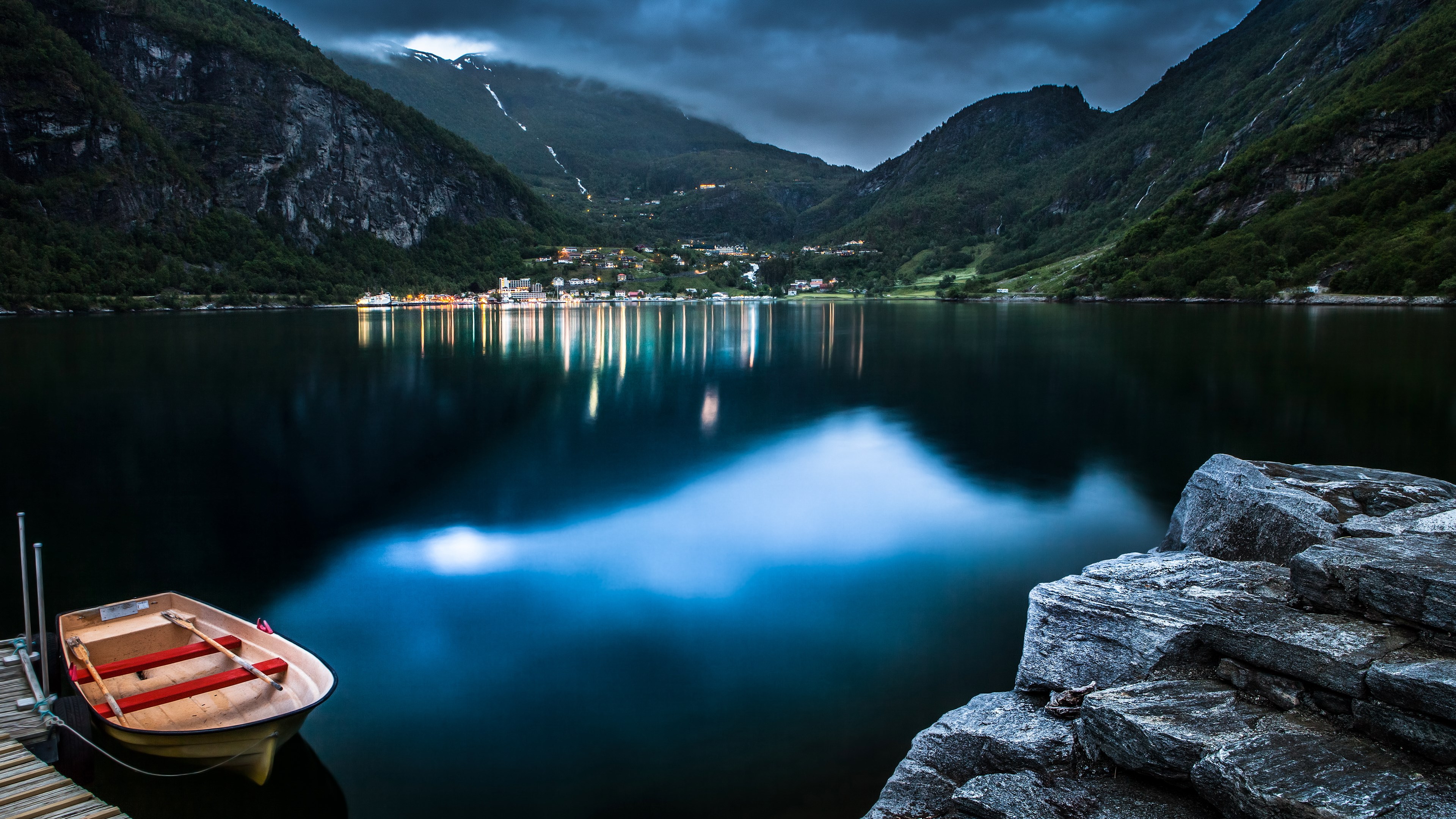 Boat docked on a lake with a village in the background HD Wallpaper