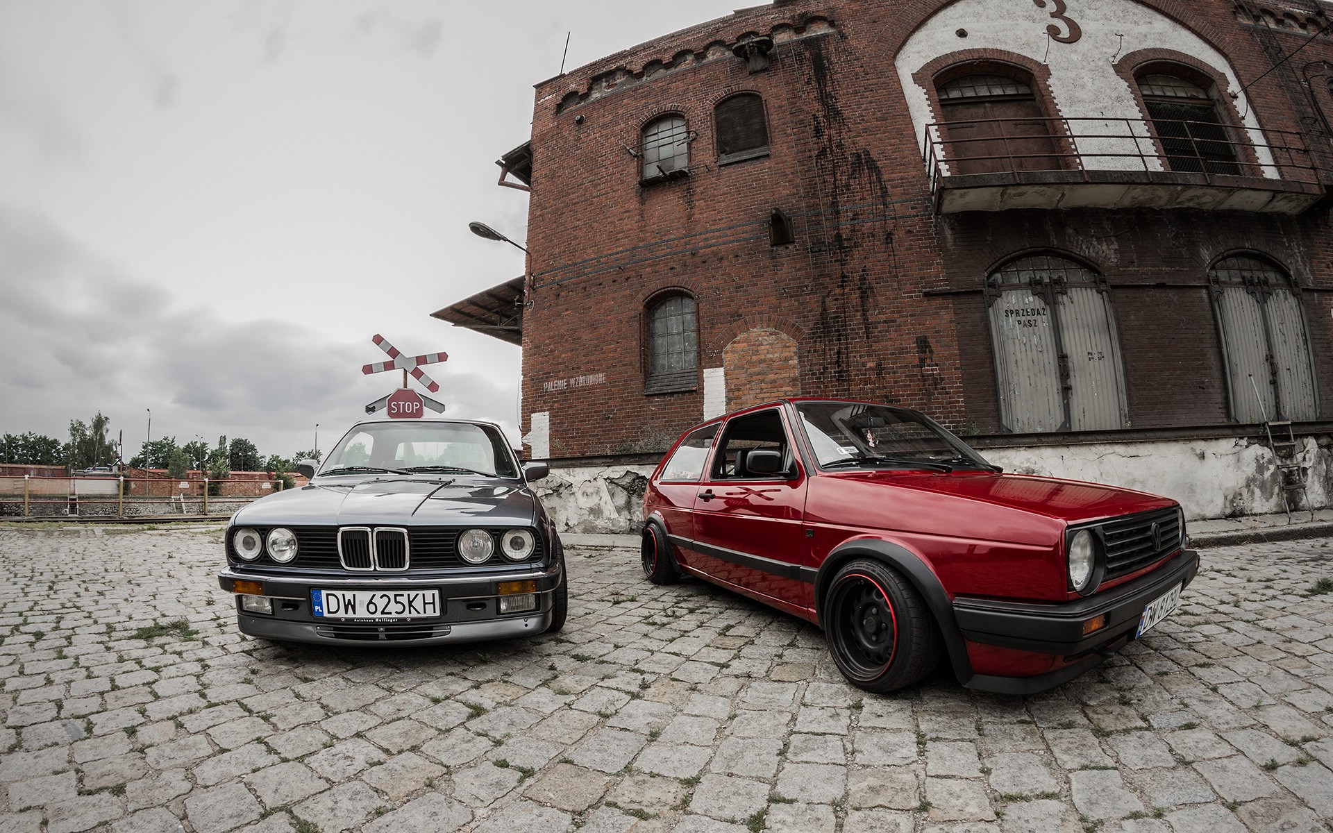 Classic BMW E30 and Volkswagen Golf parked in front of a brick building HD Wallpaper