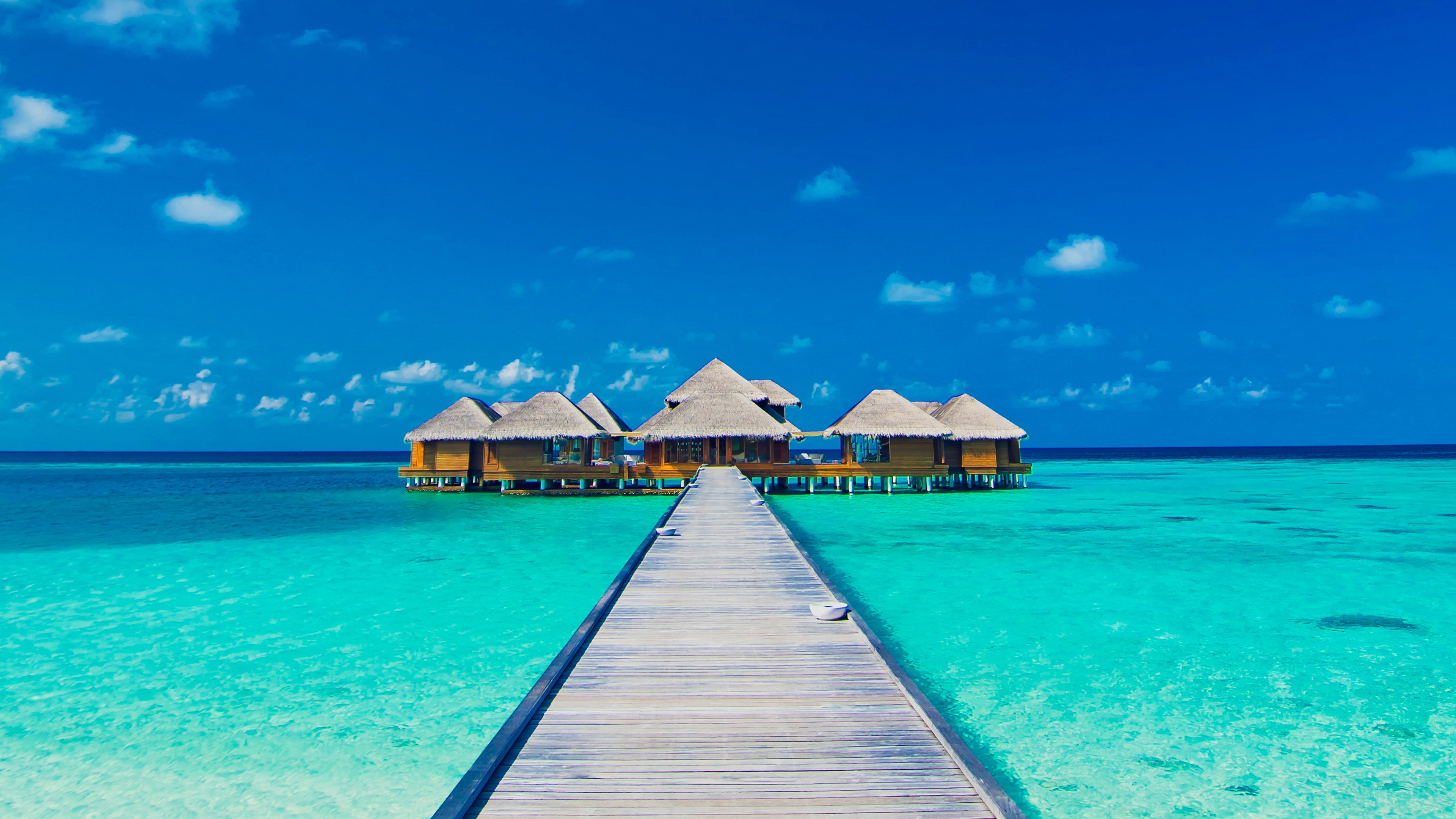 Overwater bungalows with a wooden pier in turquoise water HD Wallpaper