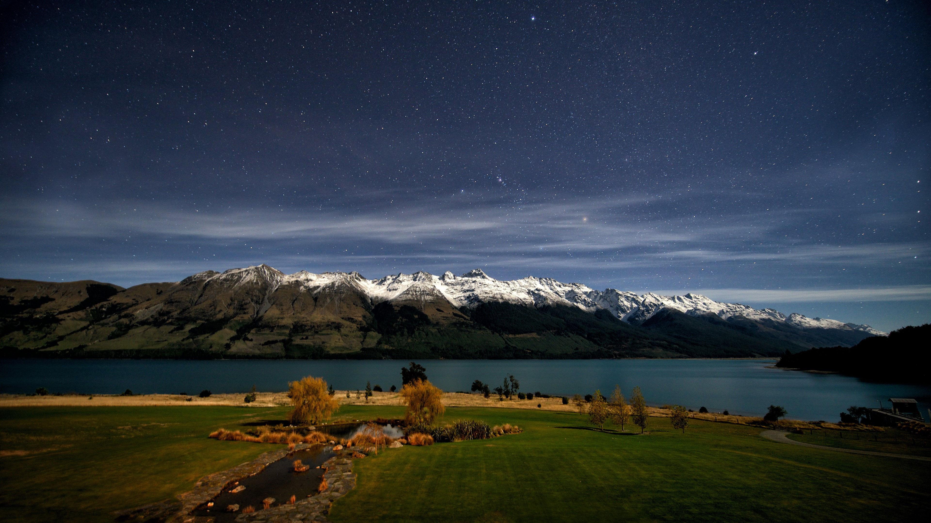 Snow-capped mountains over a lake under a starry night sky HD Wallpaper
