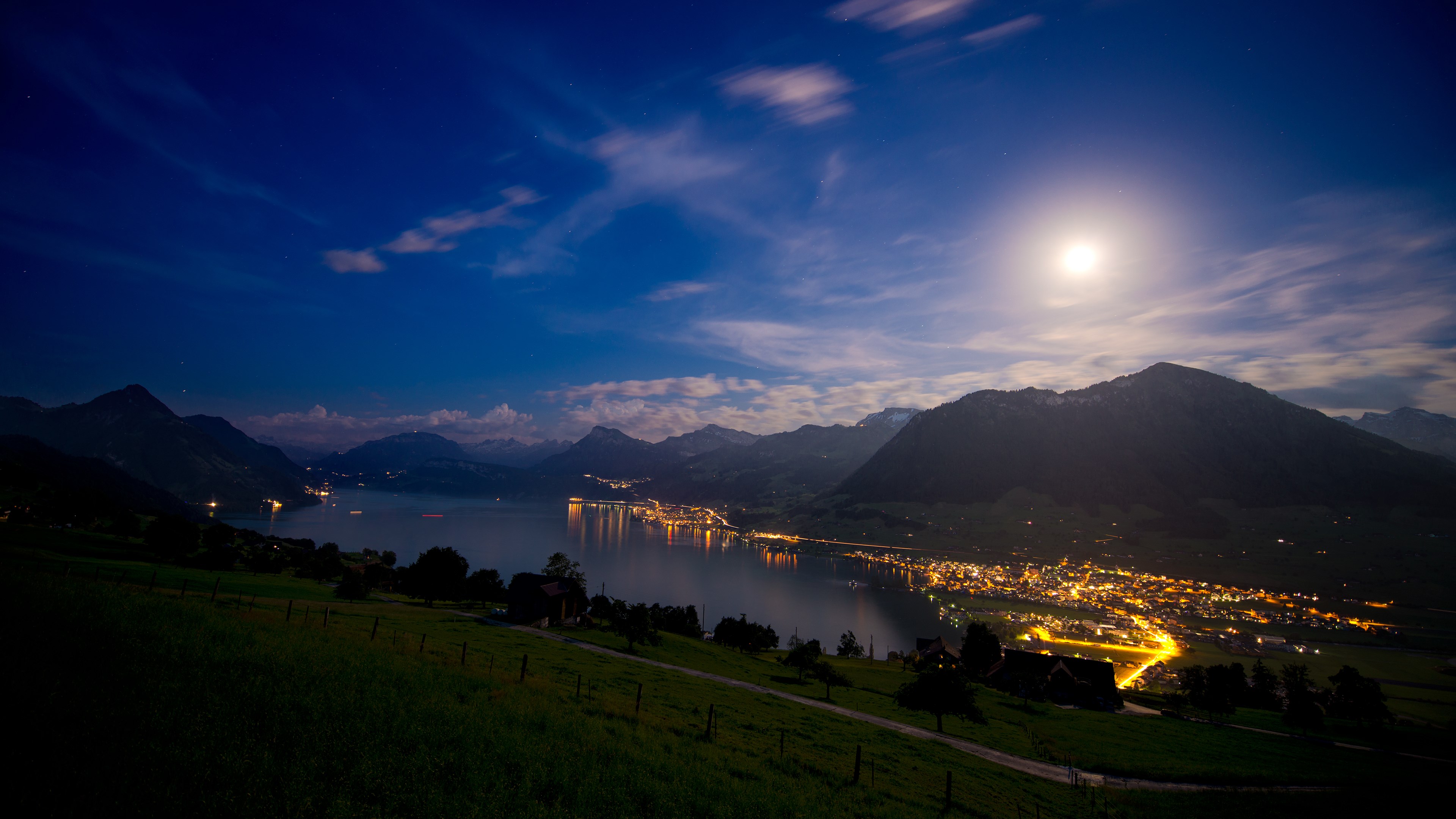 Town lights reflecting on a lake at night with mountains HD Wallpaper