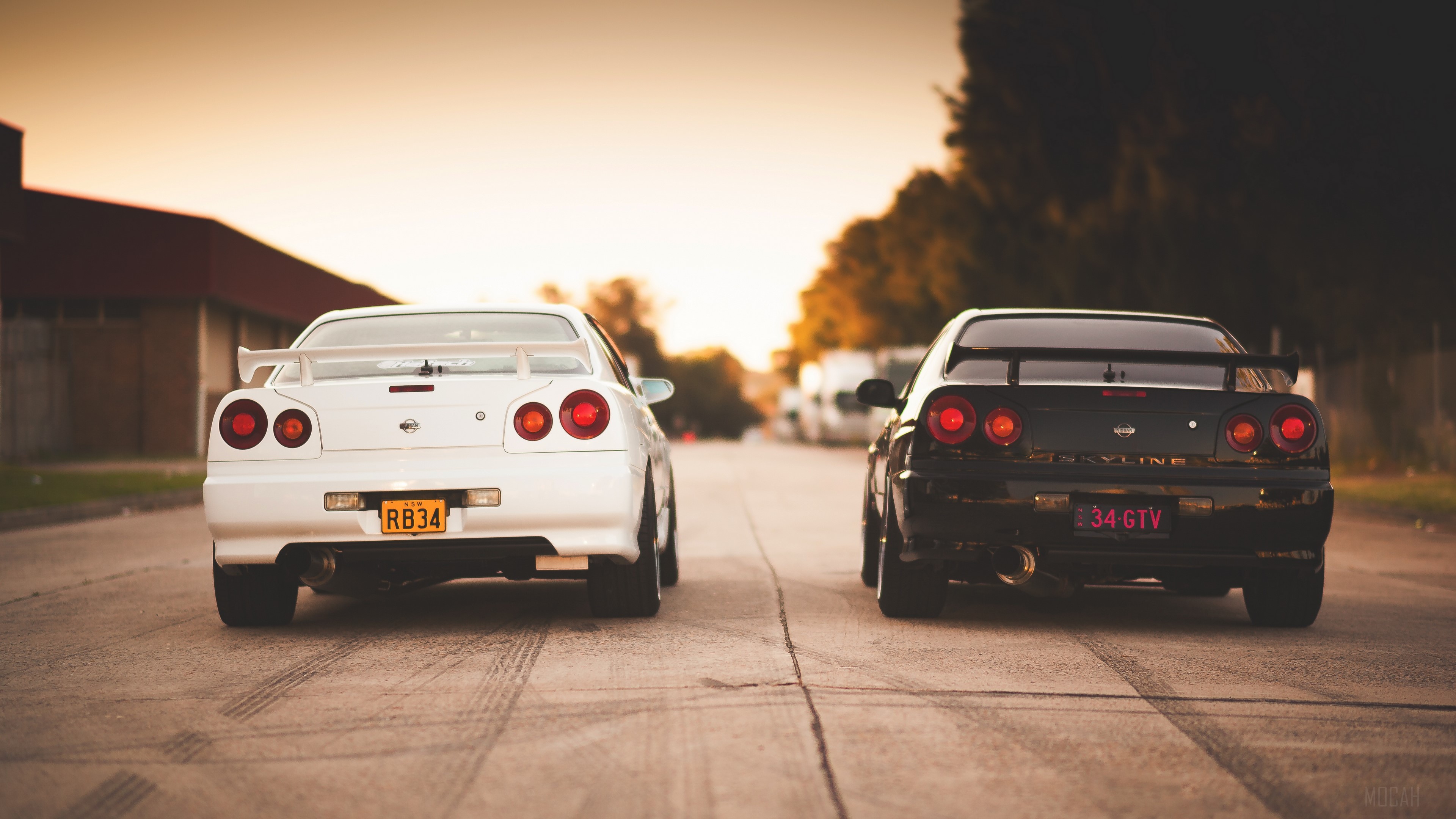 Two Nissan Skyline R34 GT-R cars on a road HD Wallpaper