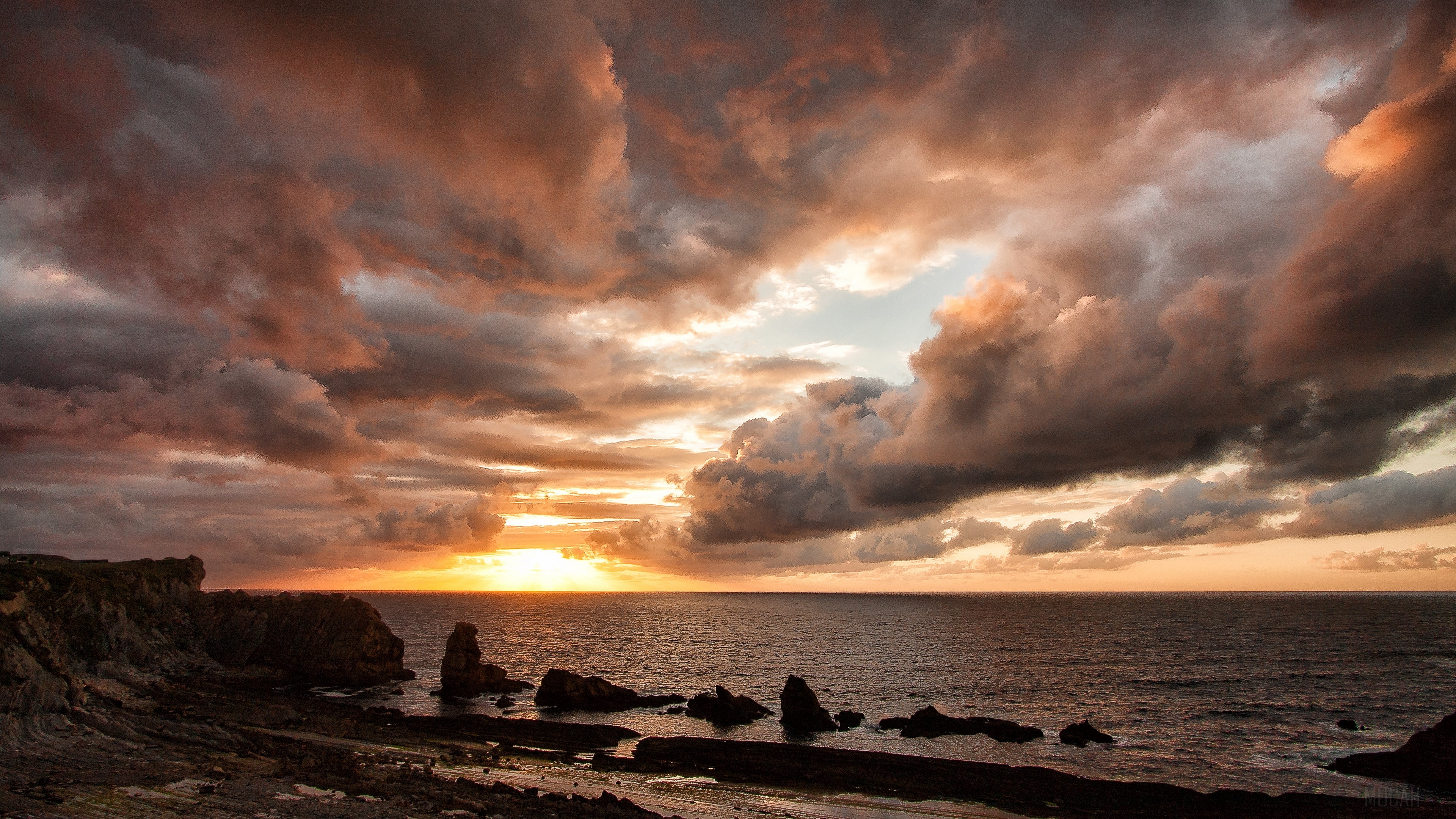 Sunset over the ocean with dramatic clouds and rocky shore HD Wallpaper