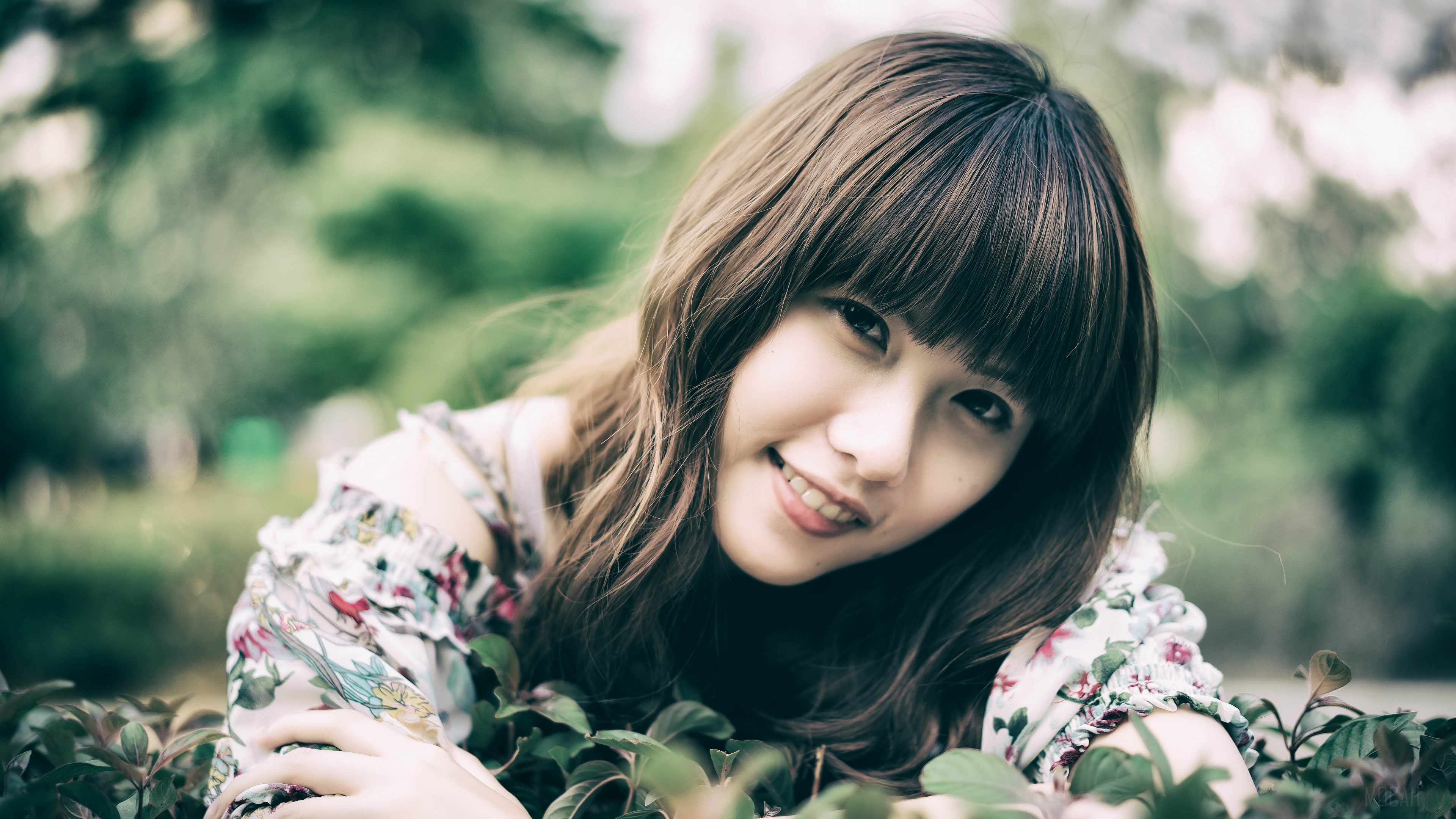 A young woman with bangs smiles in a garden HD Wallpaper