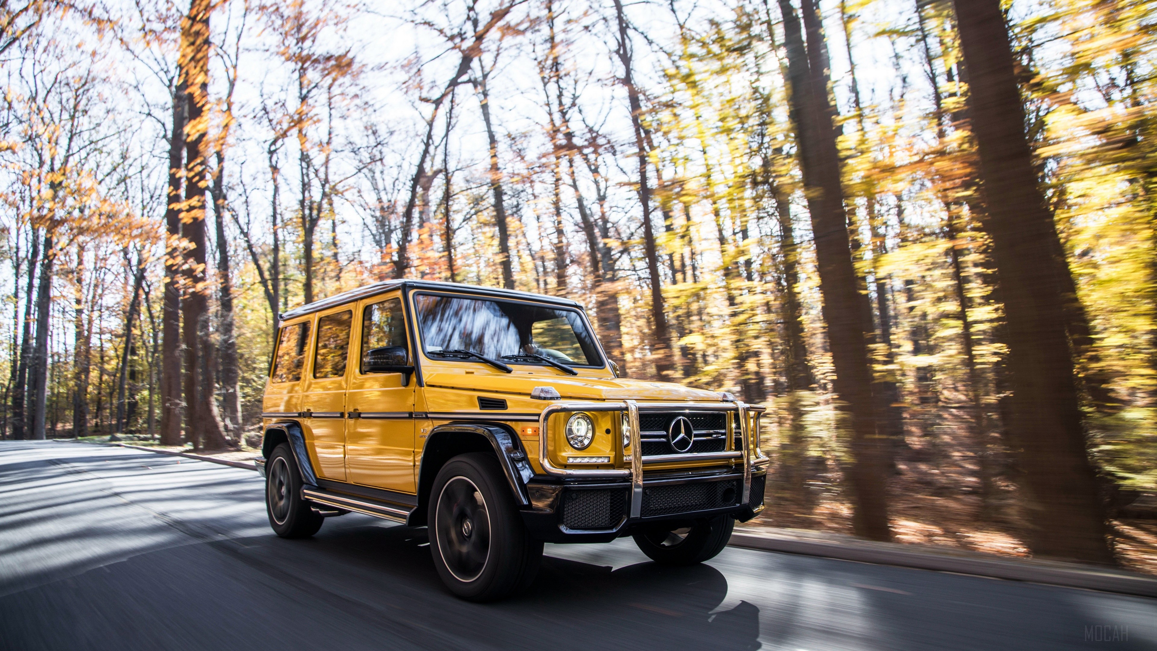 Yellow Mercedes-AMG G 63 driving on a road in autumn forest HD Wallpaper