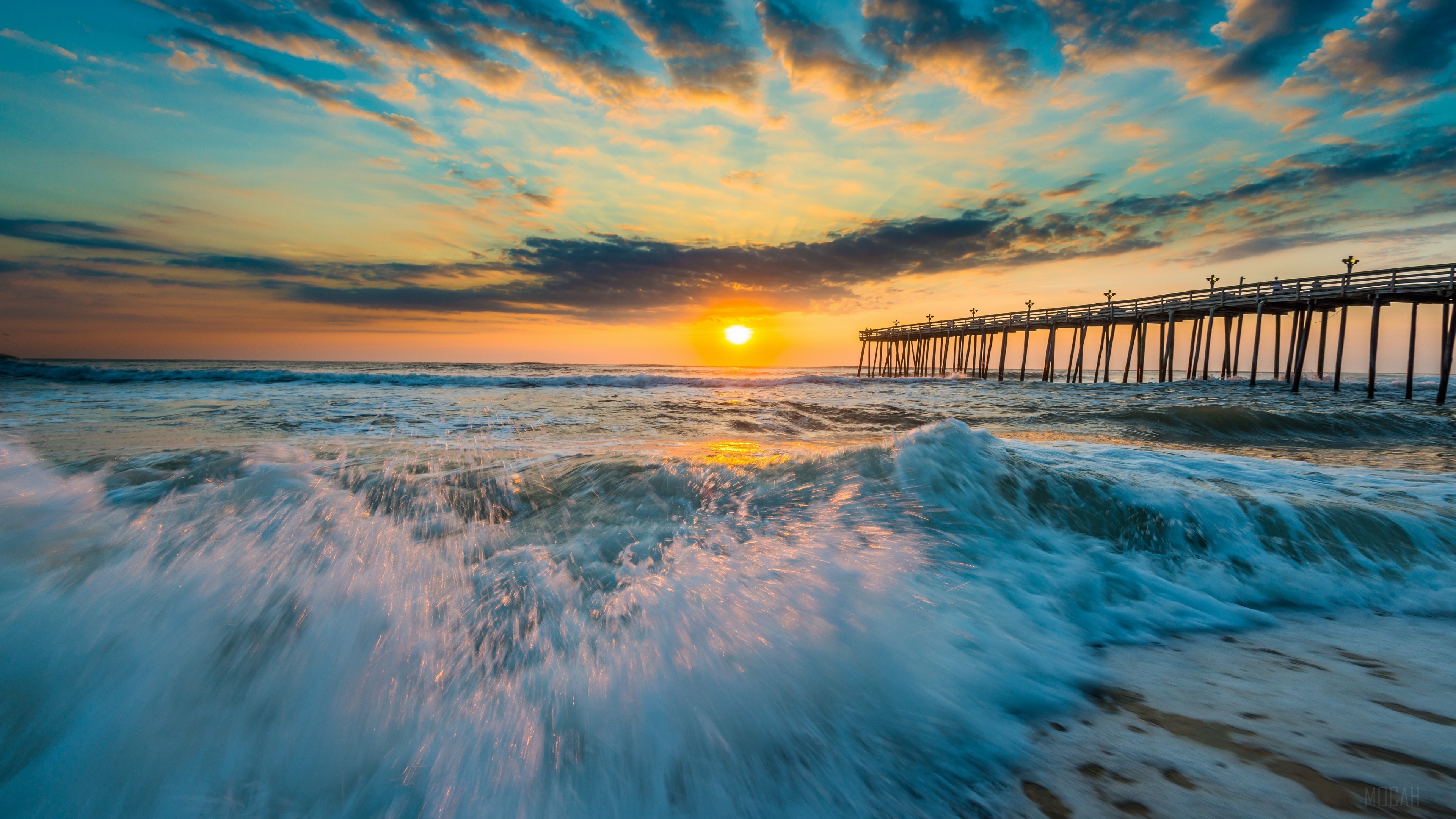 Ocean waves crash near a pier at sunset HD Wallpaper