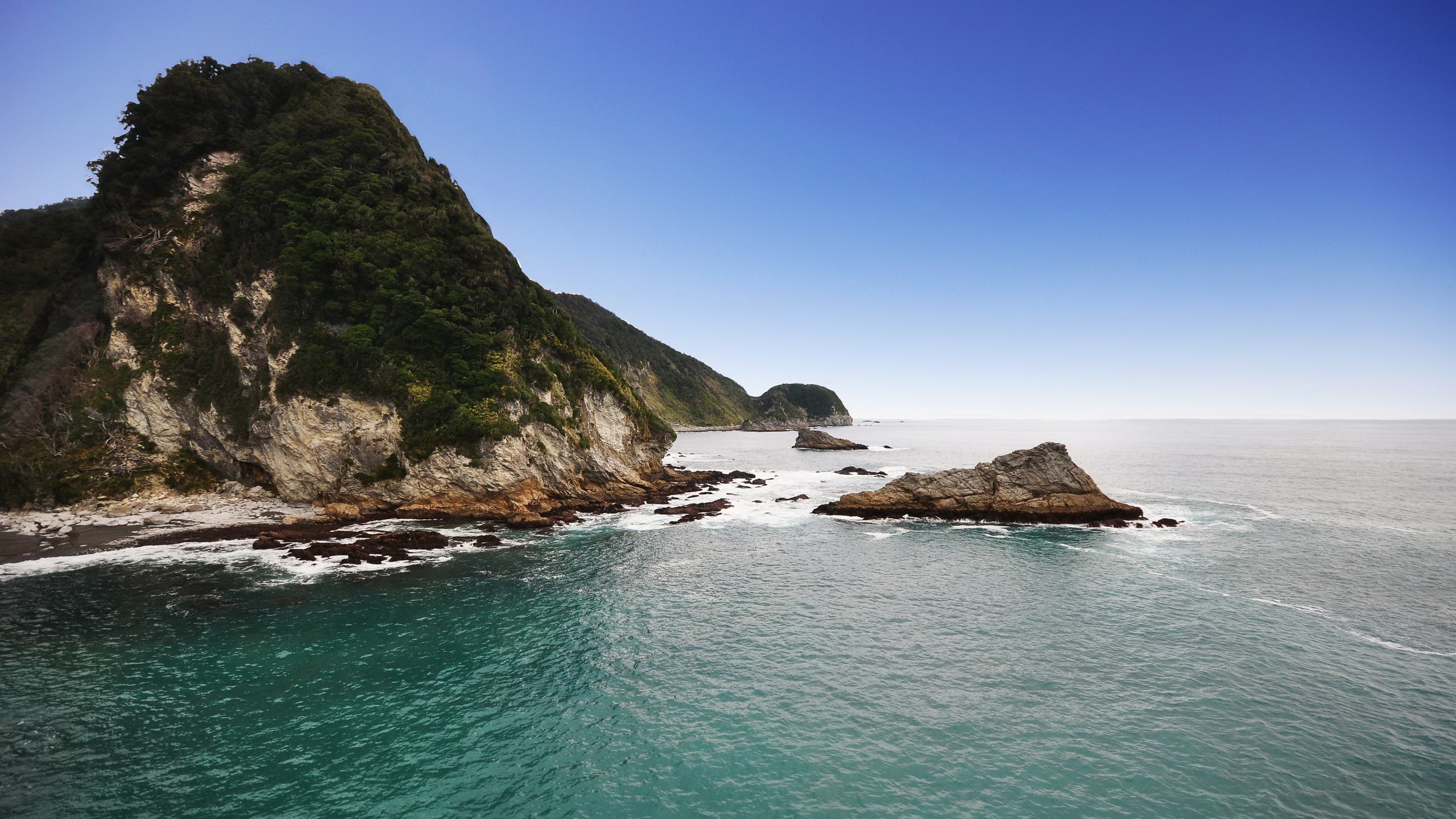 Rocky coastline with green mountains and blue sky HD Wallpaper