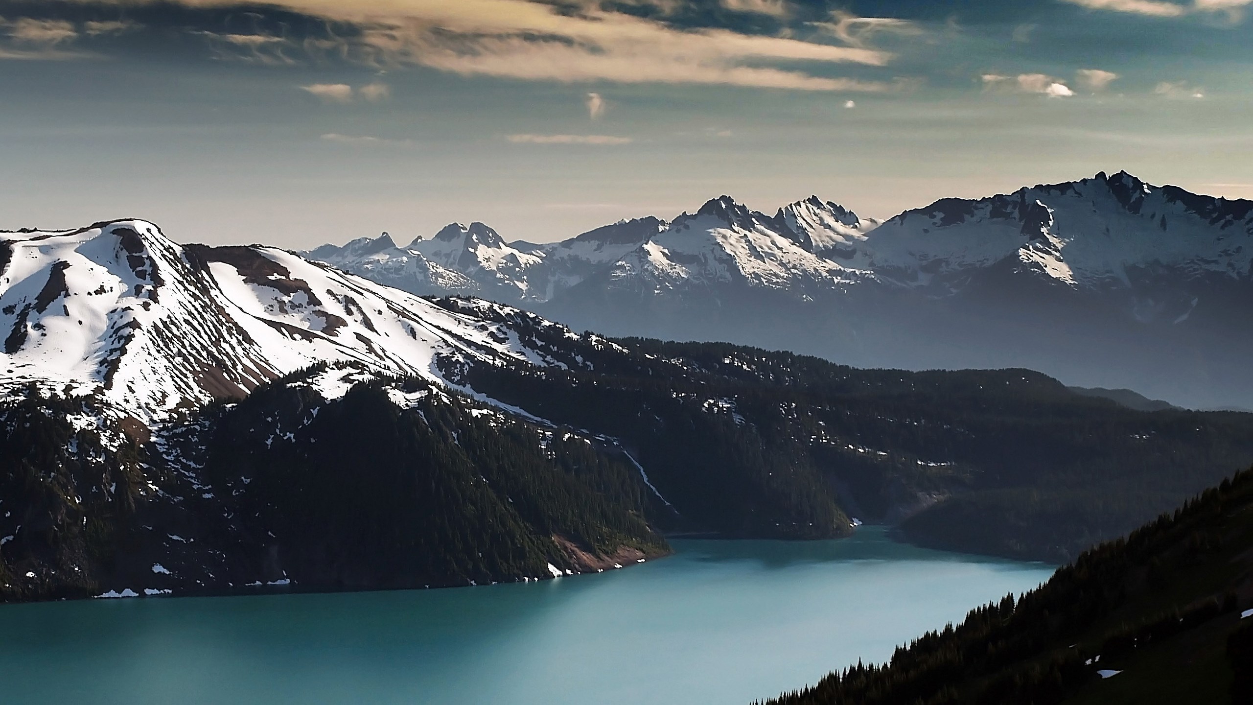 Turquoise lake surrounded by snow-capped mountains and dark forests HD Wallpaper