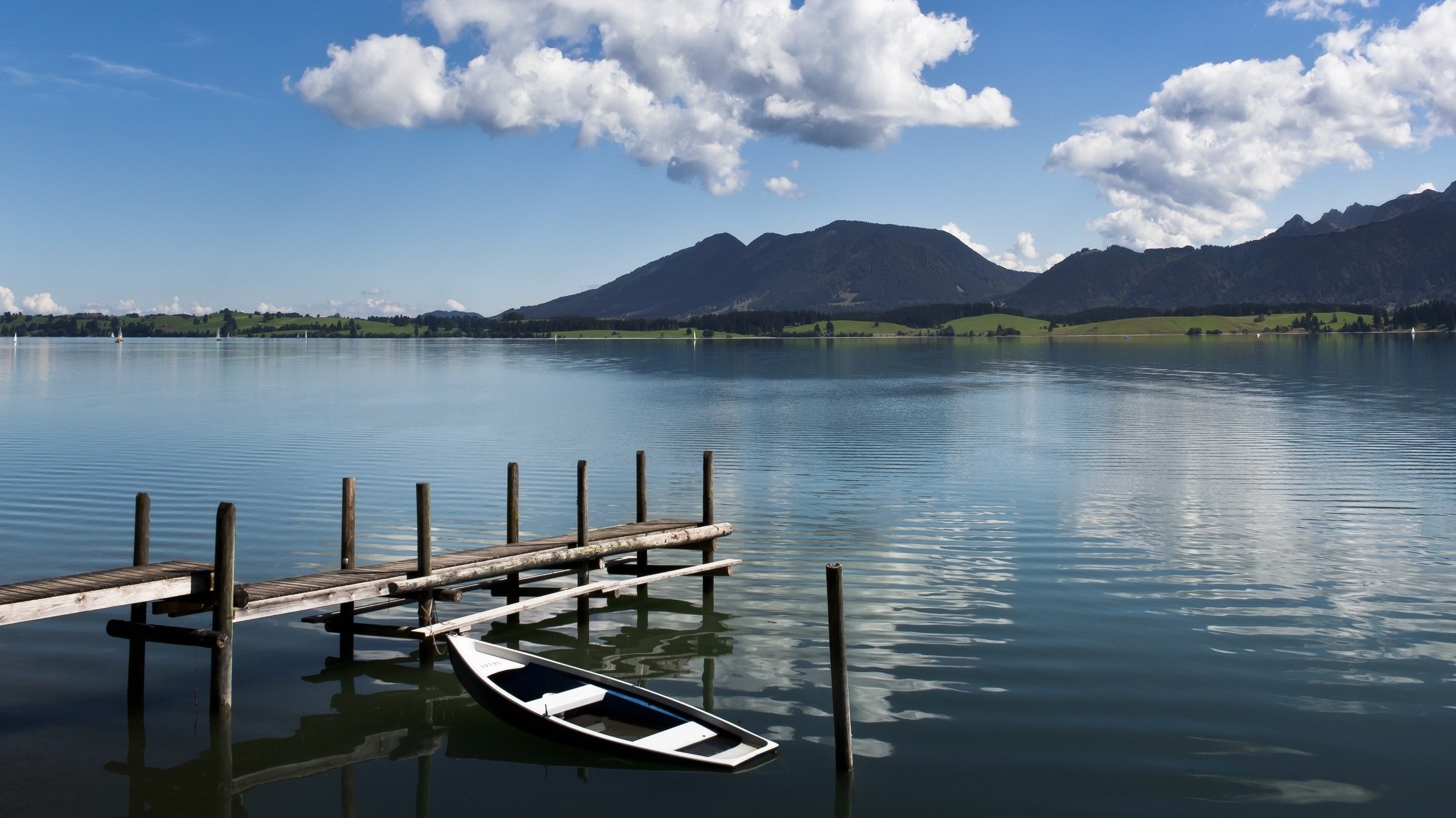 Wooden dock and rowboat on a calm lake with mountains HD Wallpaper