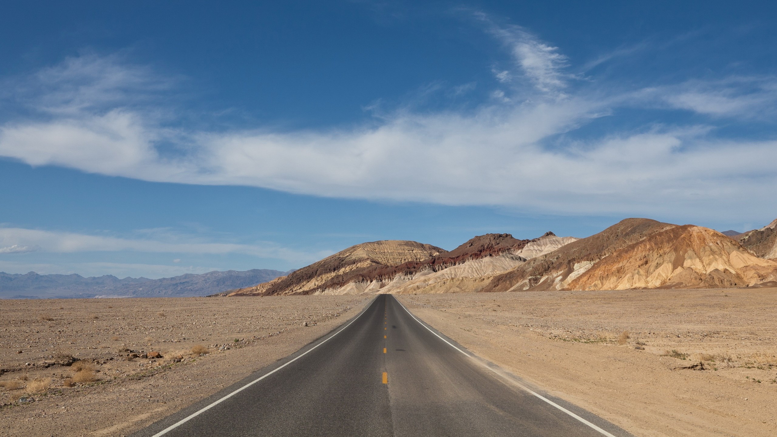 Desert road leading to colorful mountains under a blue sky HD Wallpaper
