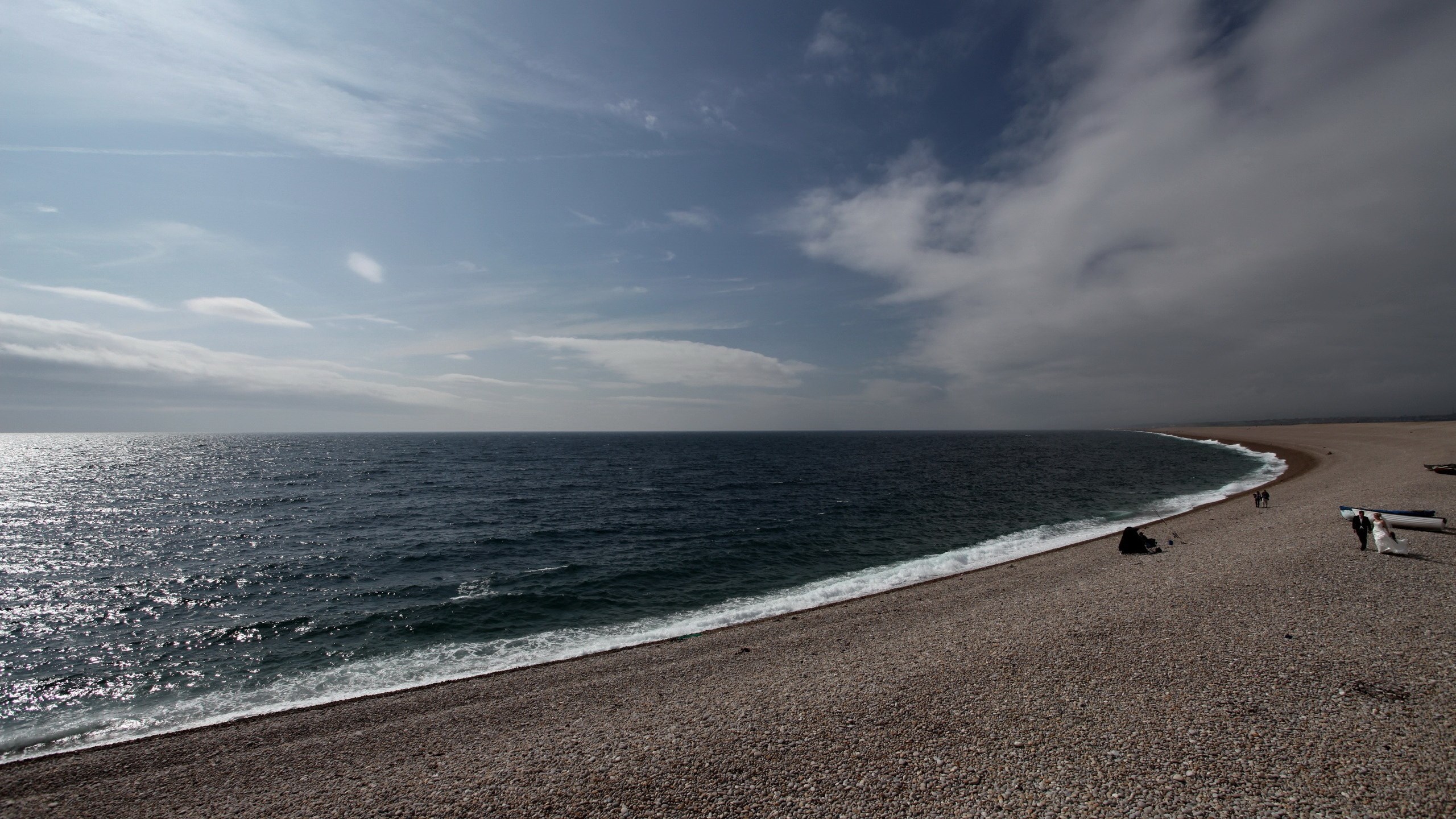 Couple walking on a pebble beach with the sea and sky HD Wallpaper
