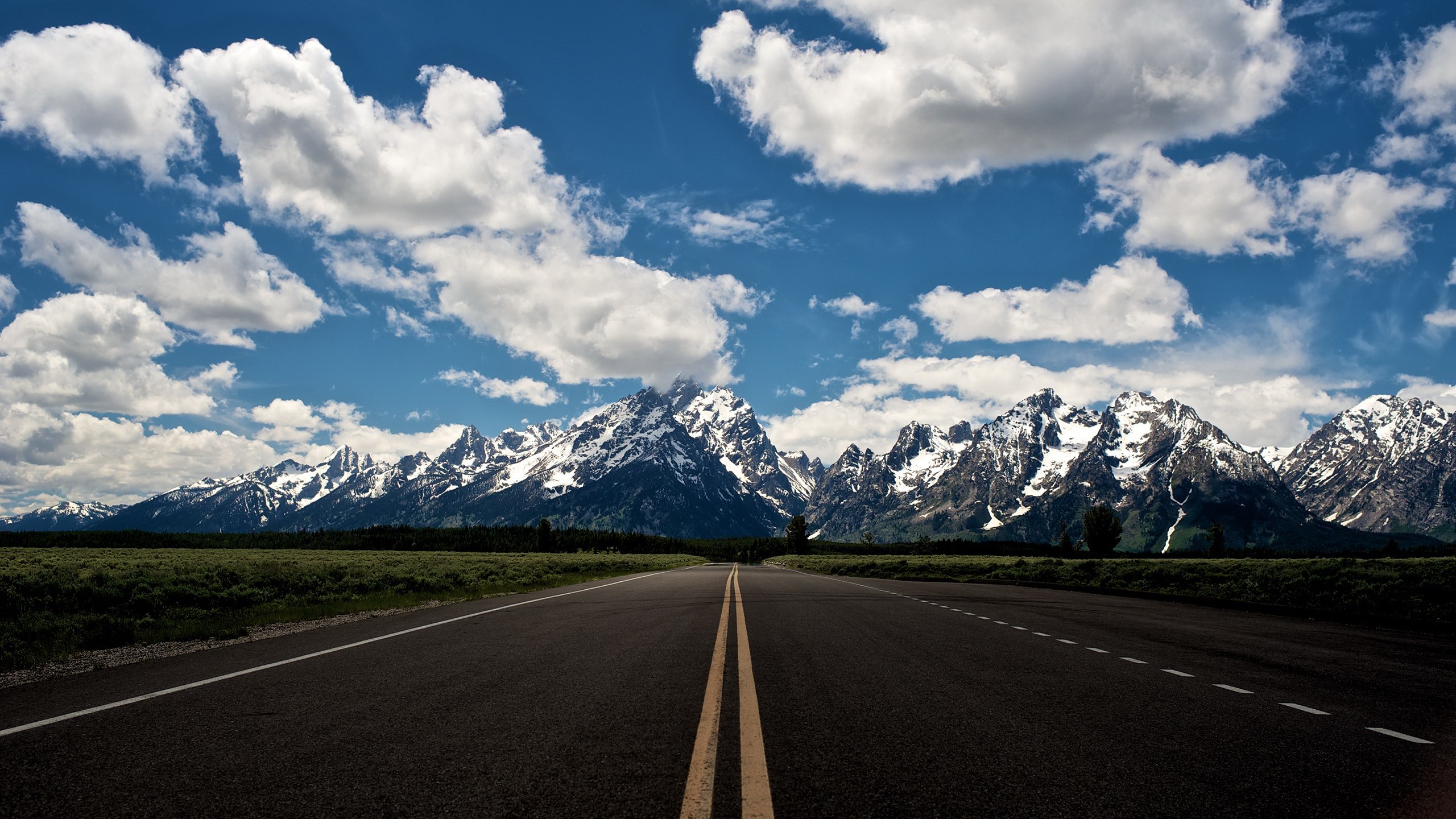 Road leading to snow-capped mountains under a cloudy sky HD Wallpaper