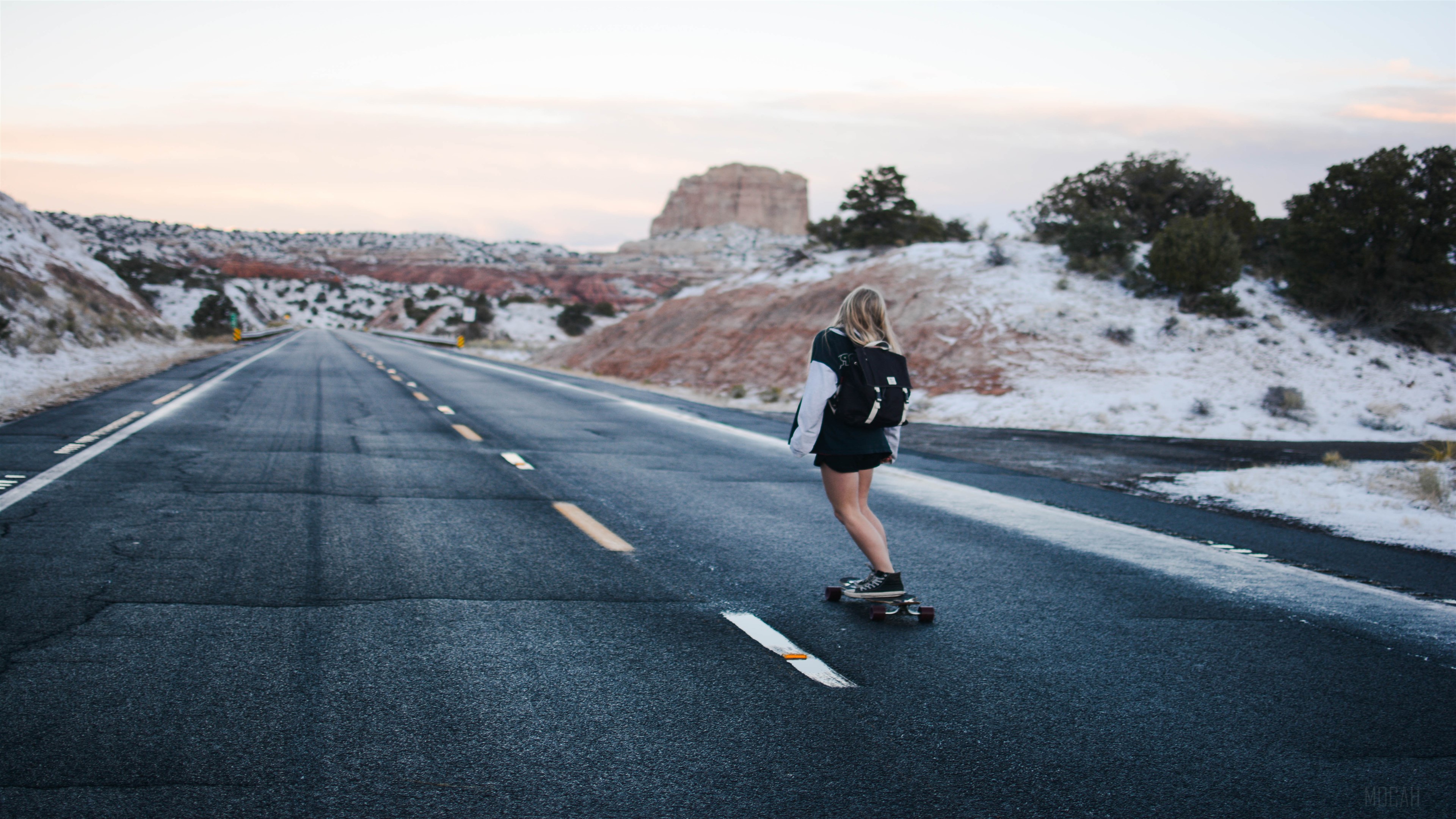 Girl skateboarding on a road with snow-covered hills HD Wallpaper