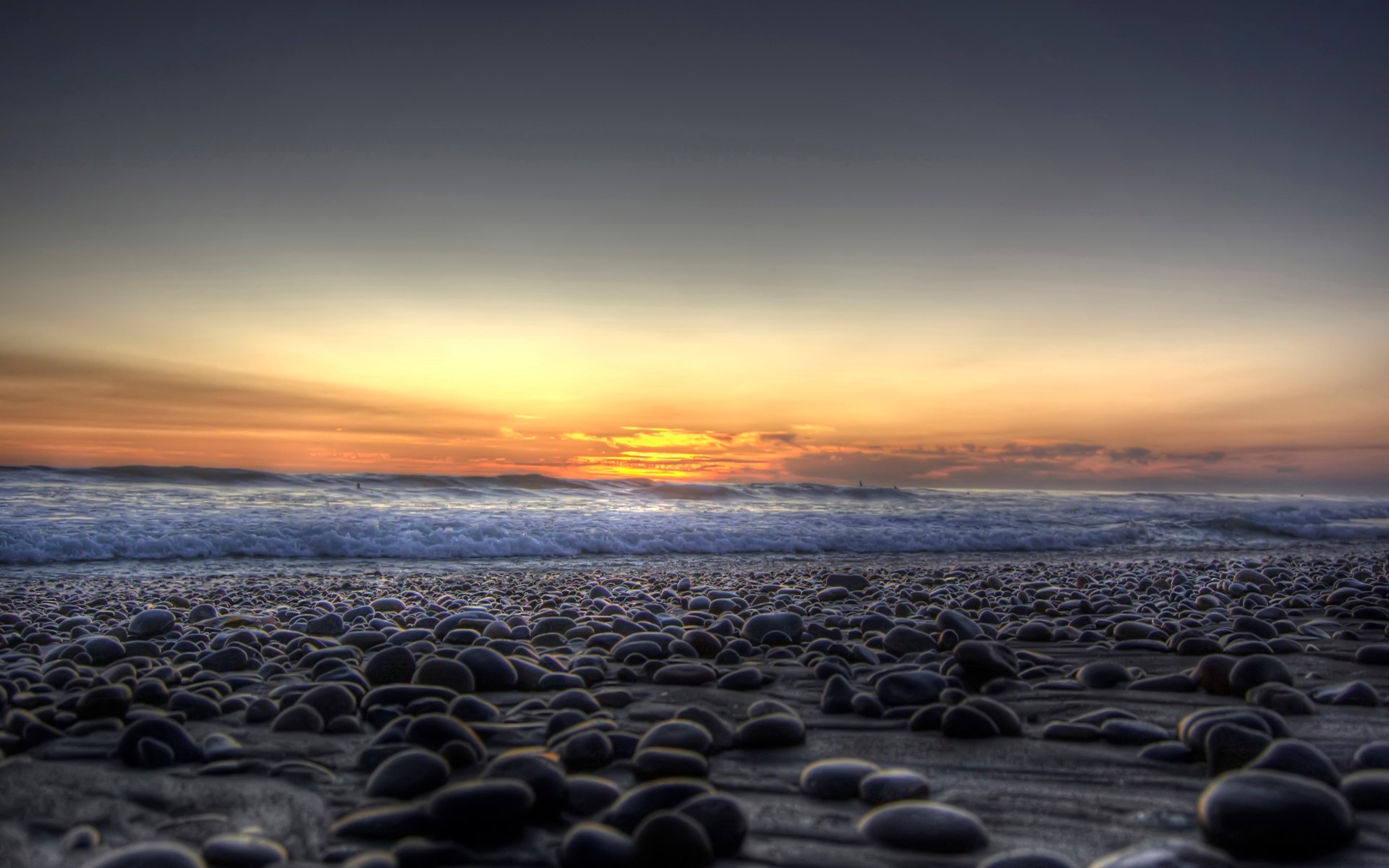 Pebble beach at sunset with ocean waves HD Wallpaper